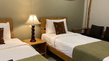 Ein Hotelzimmer mit zwei Betten, einem Holzkopfteil, einem Nachttisch mit Lampe und einer grünen Decke auf einem Bett.