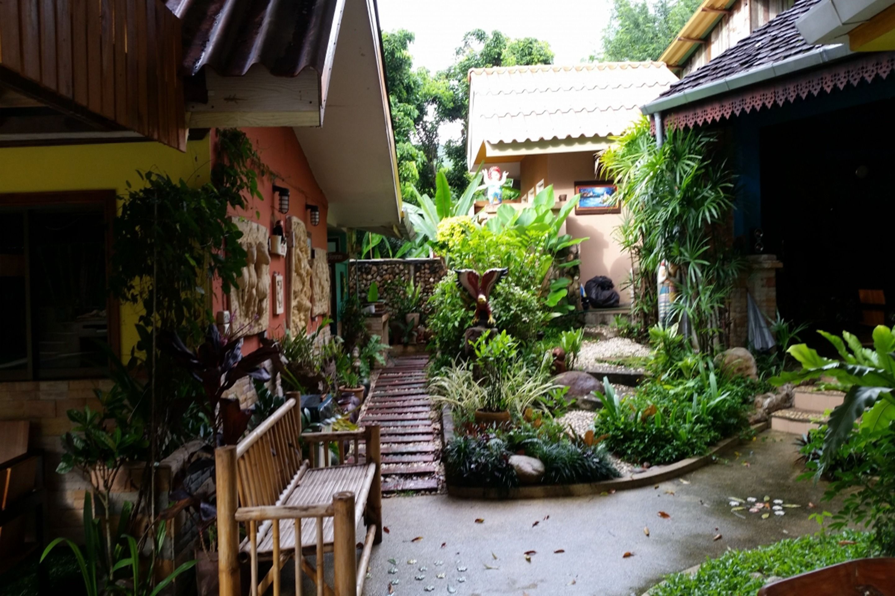 A courtyard with a wooden bench, potted plants, and a stone pathway.
