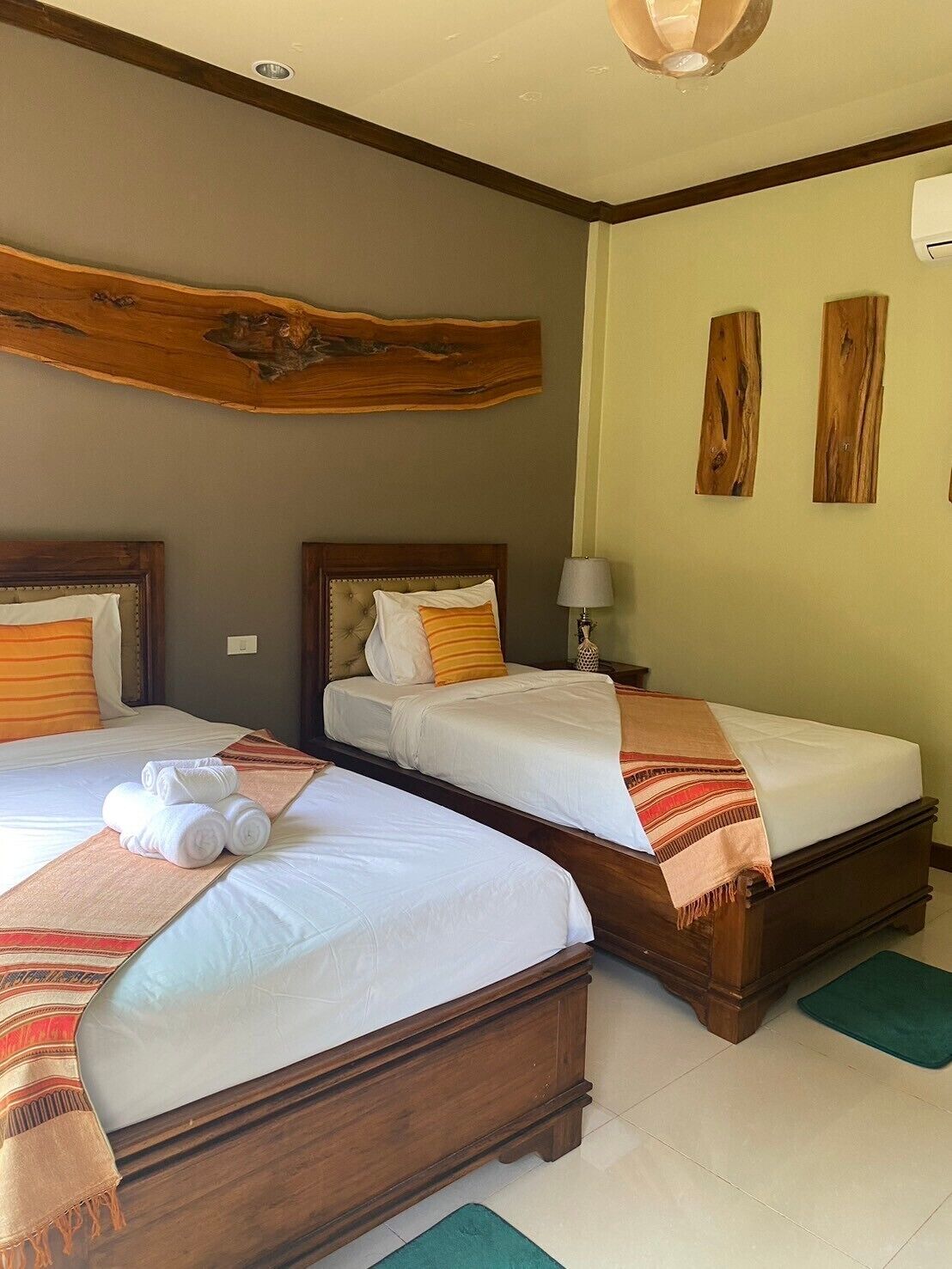 Een hotelkamer met twee bedden, houten hoofdeinden, een houten wanddecoratie, een lamp en een groene mat.