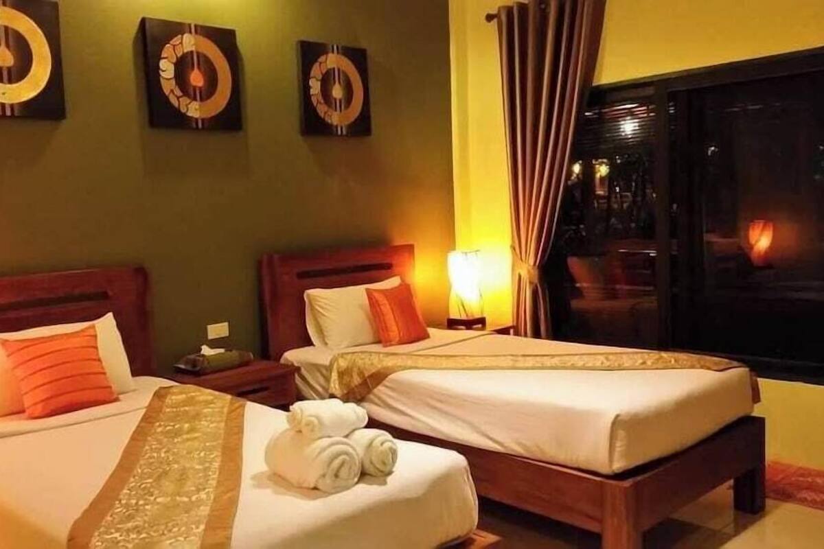 Habitación de hotel con dos camas, una mesita de noche, una lámpara y una ventana con cortinas.