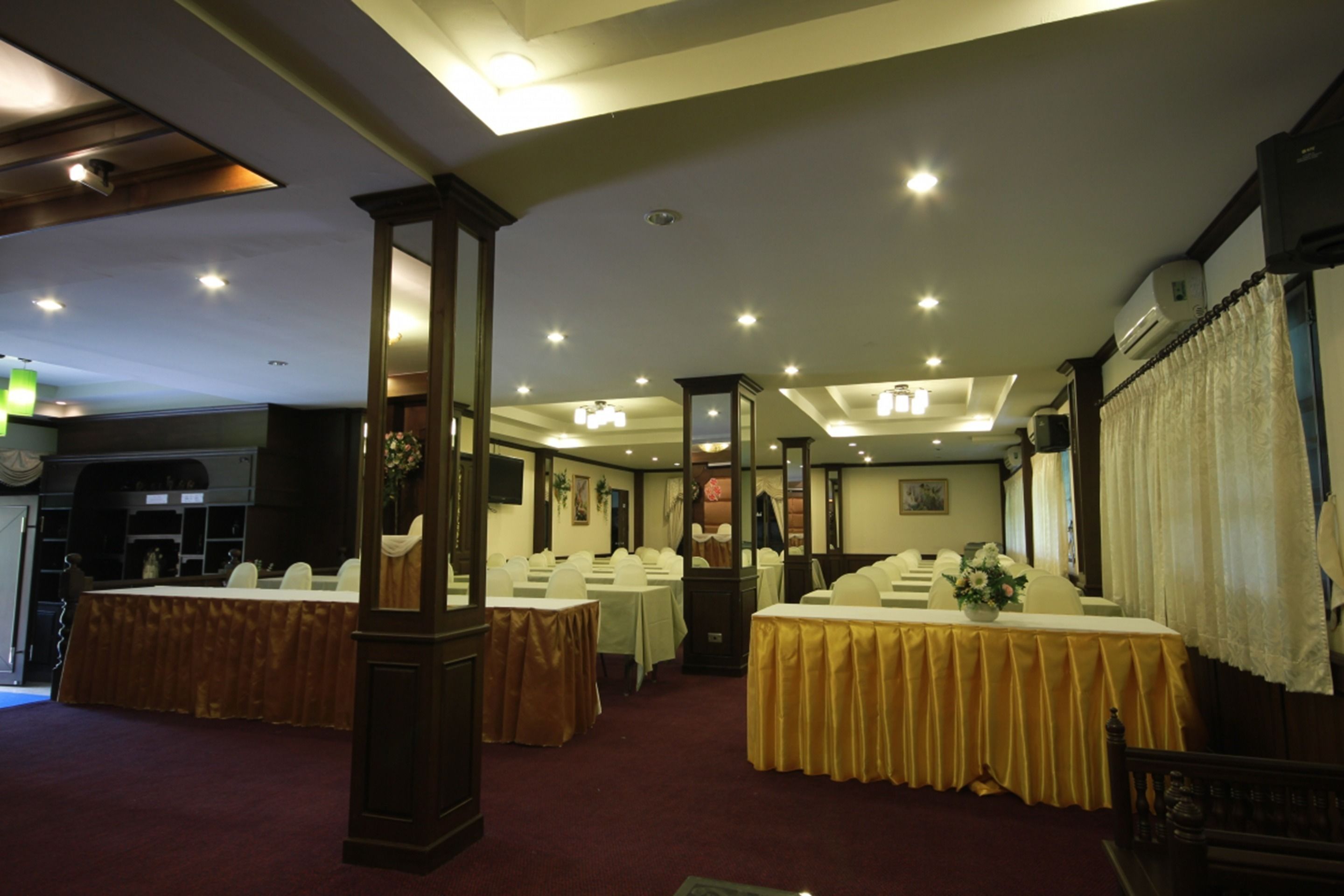 Un salón de banquetes con varias mesas dispuestas para eventos, un espejo grande y una araña.