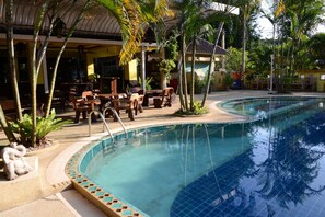 Un espace piscine avec une bordure carrelée, des chaises longues et un coin salon couvert équipé de tables et de chaises.