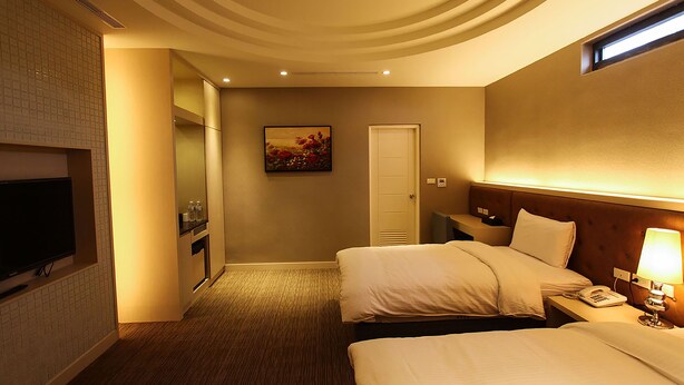 Una habitación de hotel con dos camas, un televisor, un cuadro en la pared y una puerta.