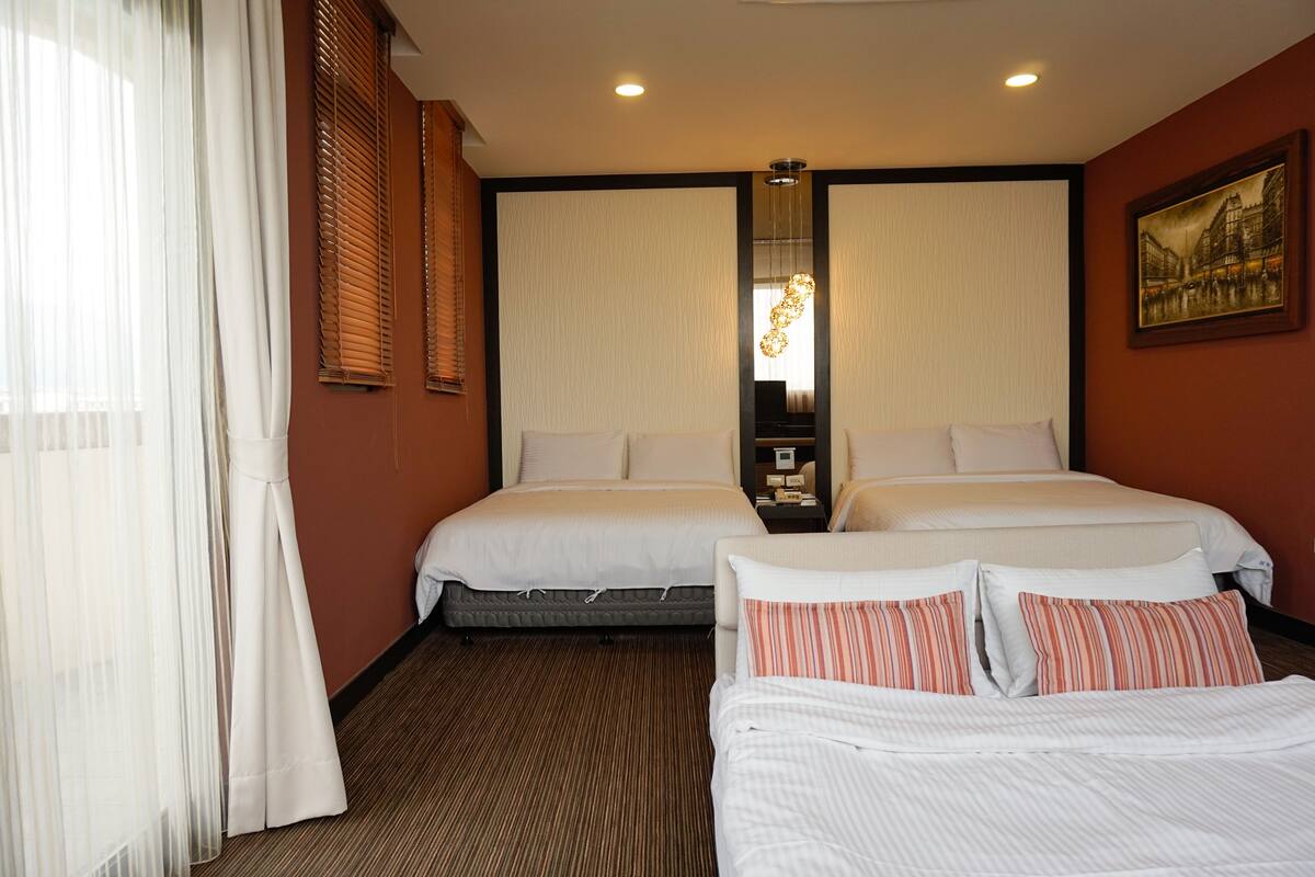 A hotel room with two beds, a large mirror, a painting on the wall, and a window with curtains.