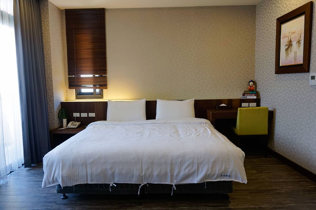 A hotel room with a large bed, a nightstand with a phone, a small table with a figurine, and a framed picture on the wall.