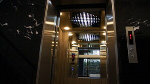Interior de un ascensor con pantalla digital, paredes metálicas y techo con diseño.