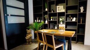 Una habitación con una mesa y sillas de madera, una puerta negra con paneles de vidrio esmerilado y una estantería llena de objetos decorativos.