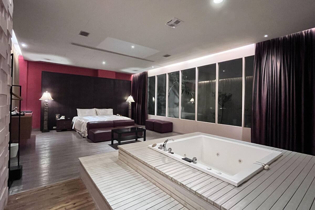 Un dormitorio moderno con una cama grande, una zona de estar, una bañera y un ventanal con cortinas.