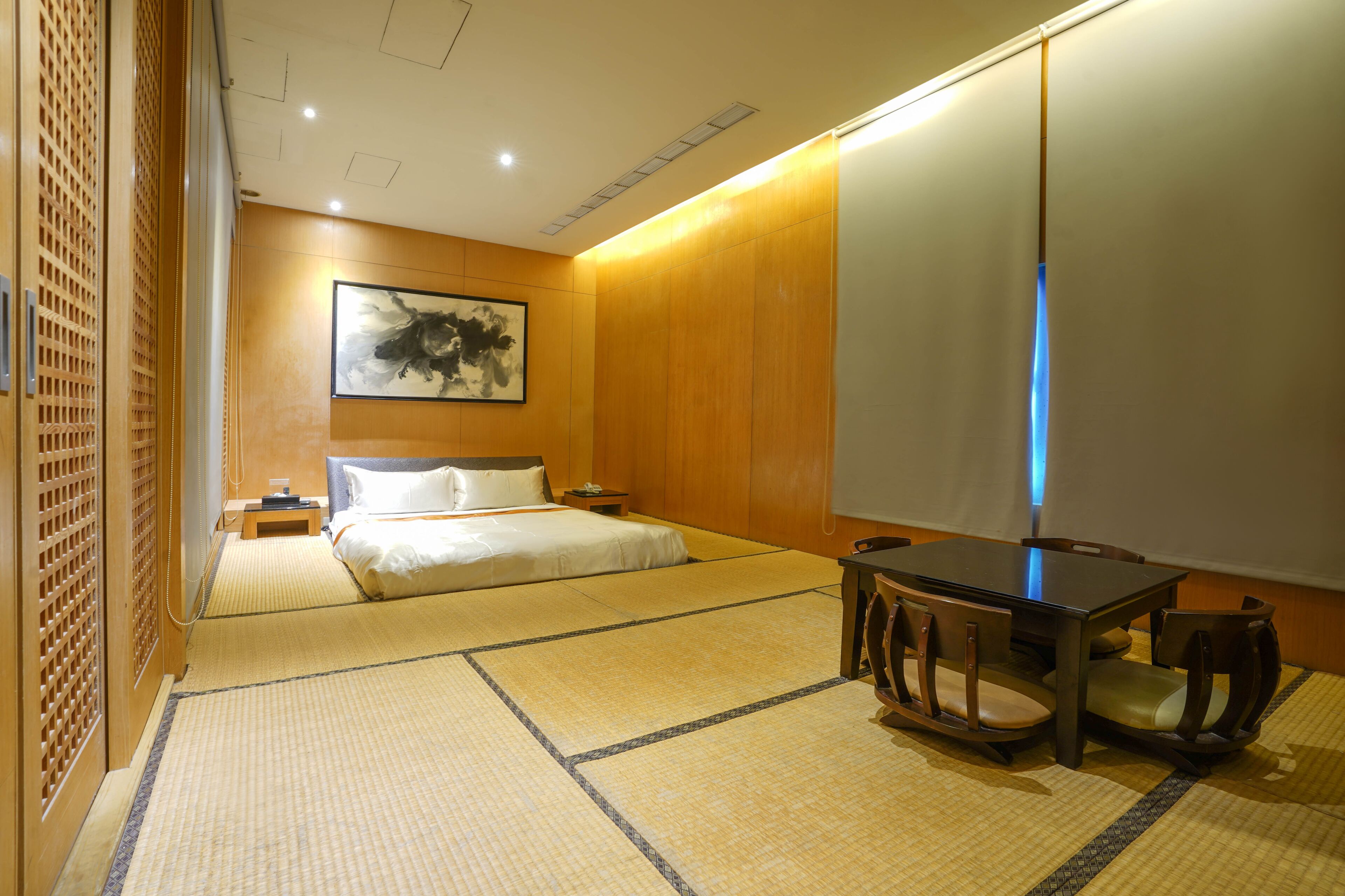 A traditional Japanese-style room with tatami flooring, a low table with chairs, a bed with white bedding, and a wall-mounted artwork.