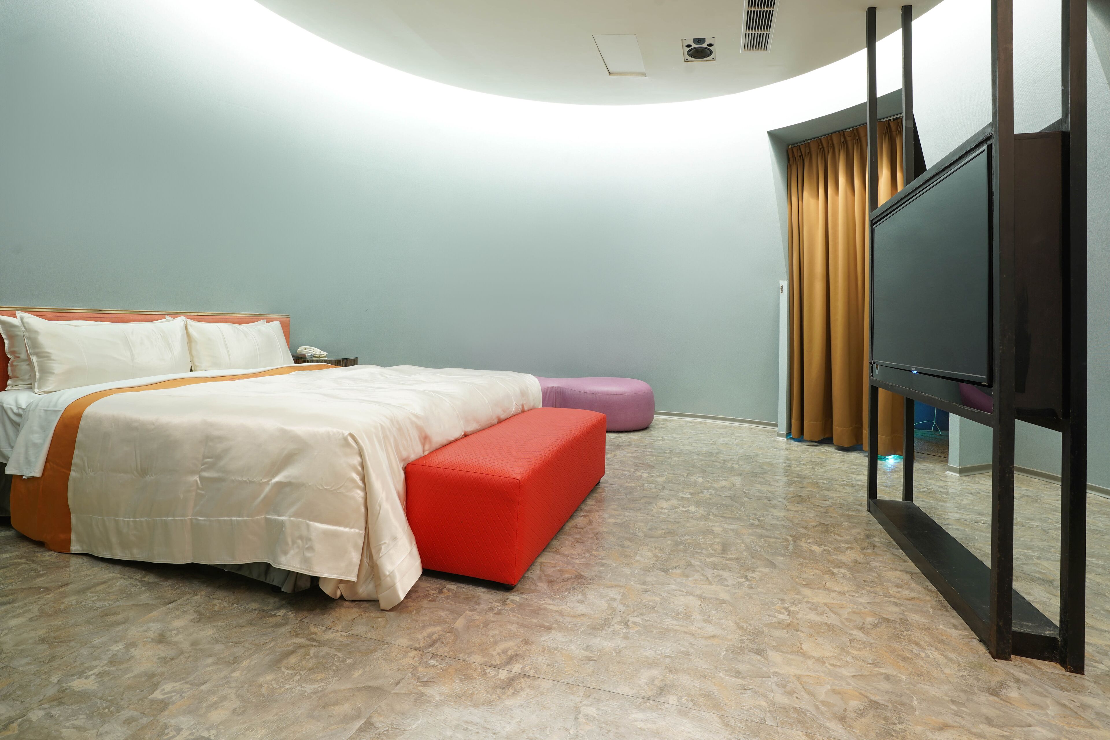 A hotel room with a bed, a TV, a small table, and a window with curtains.