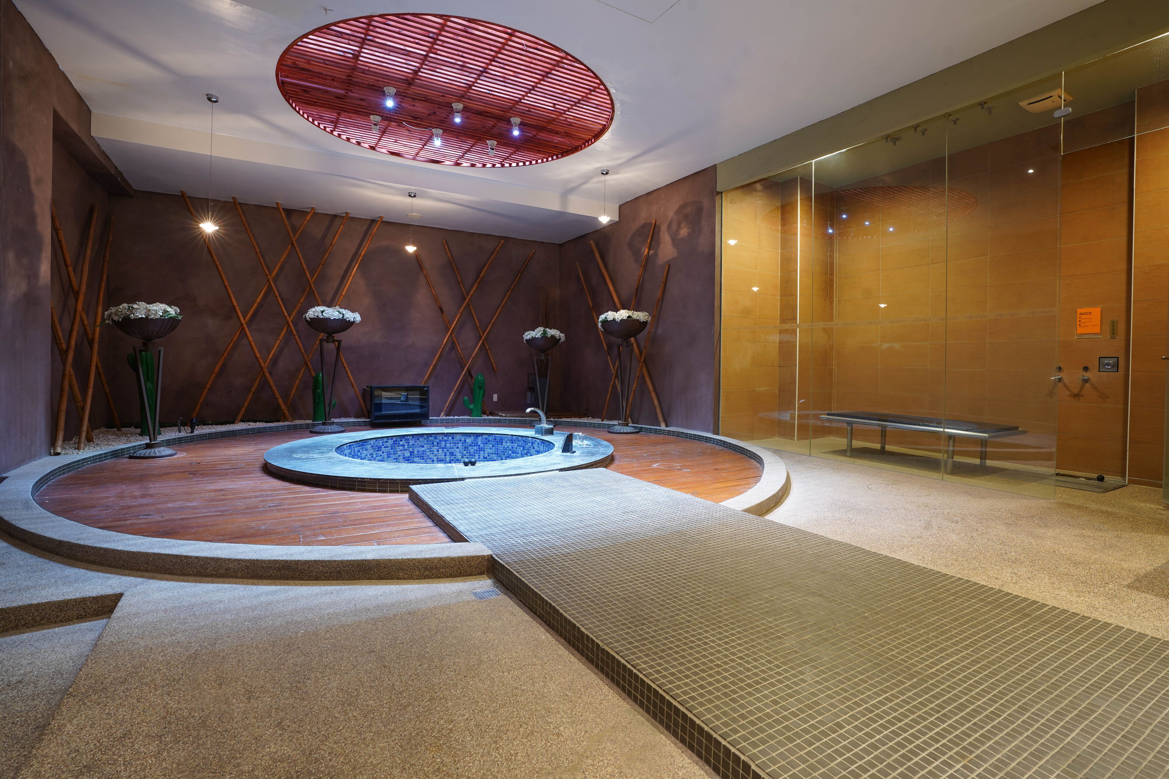 A modern indoor pool area with a central hot tub, surrounded by a wooden floor and a tiled walkway.