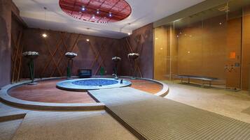 A modern indoor pool area with a central hot tub, surrounded by a wooden floor and a tiled walkway.