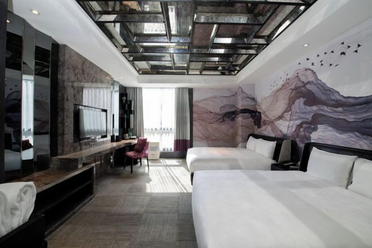 Una habitación de hotel moderna con una cama grande, un televisor y un mural en la pared.