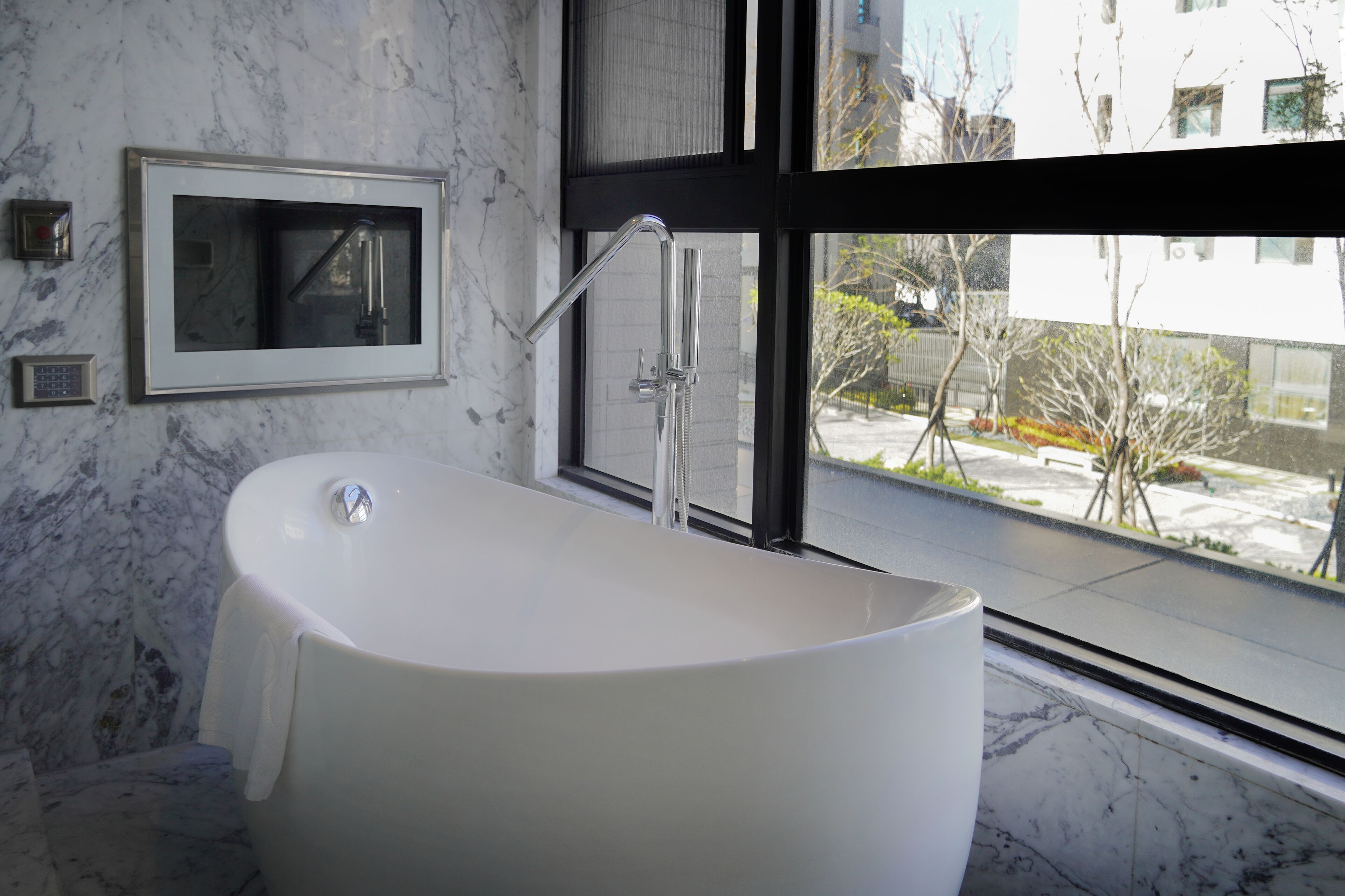 Une salle de bain moderne avec une baignoire sur pieds, un miroir fixé au mur et une fenêtre donnant sur l’extérieur.