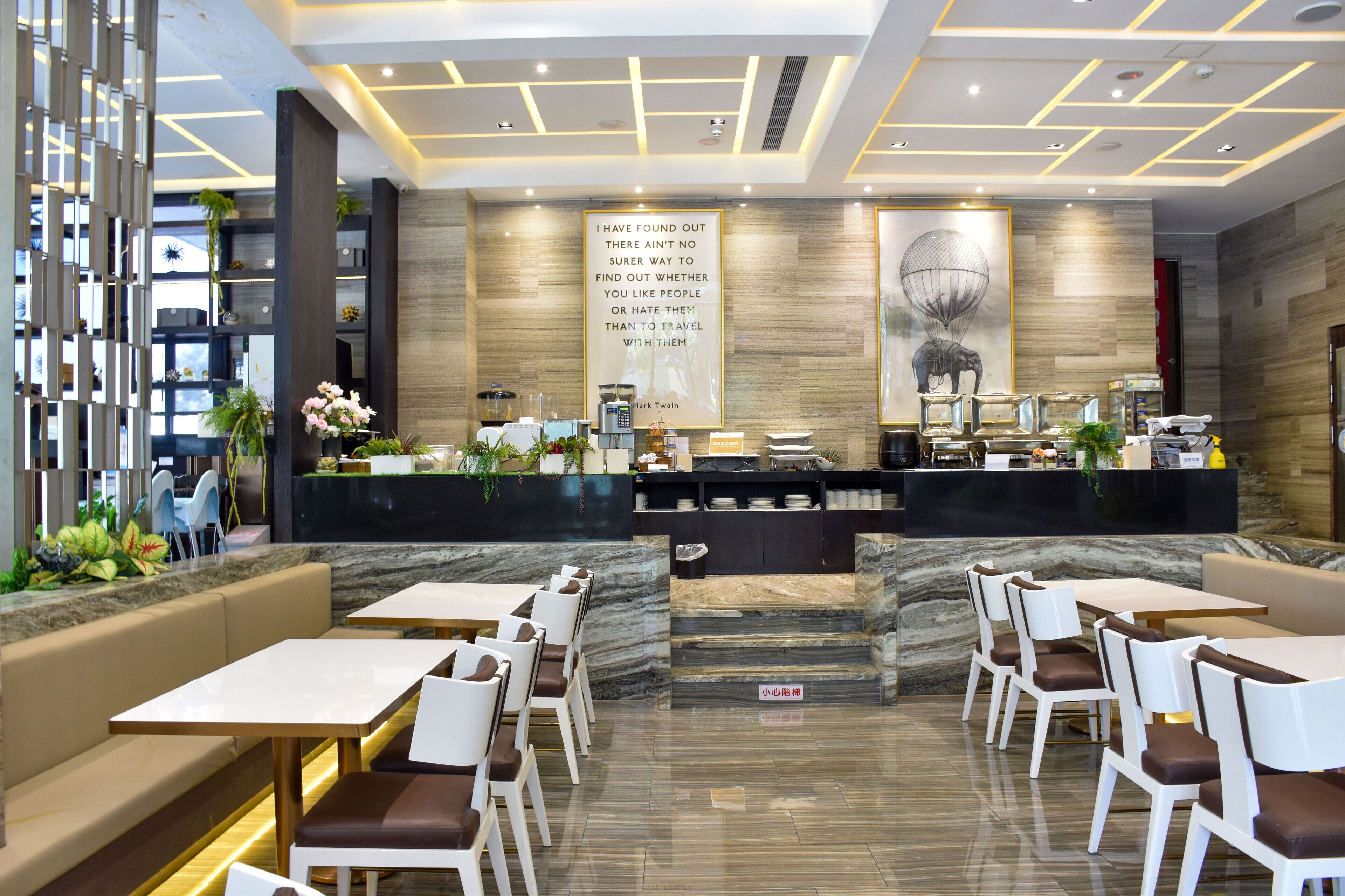 A modern restaurant with marble flooring, white and brown seating, and a central counter with a quote on the wall.