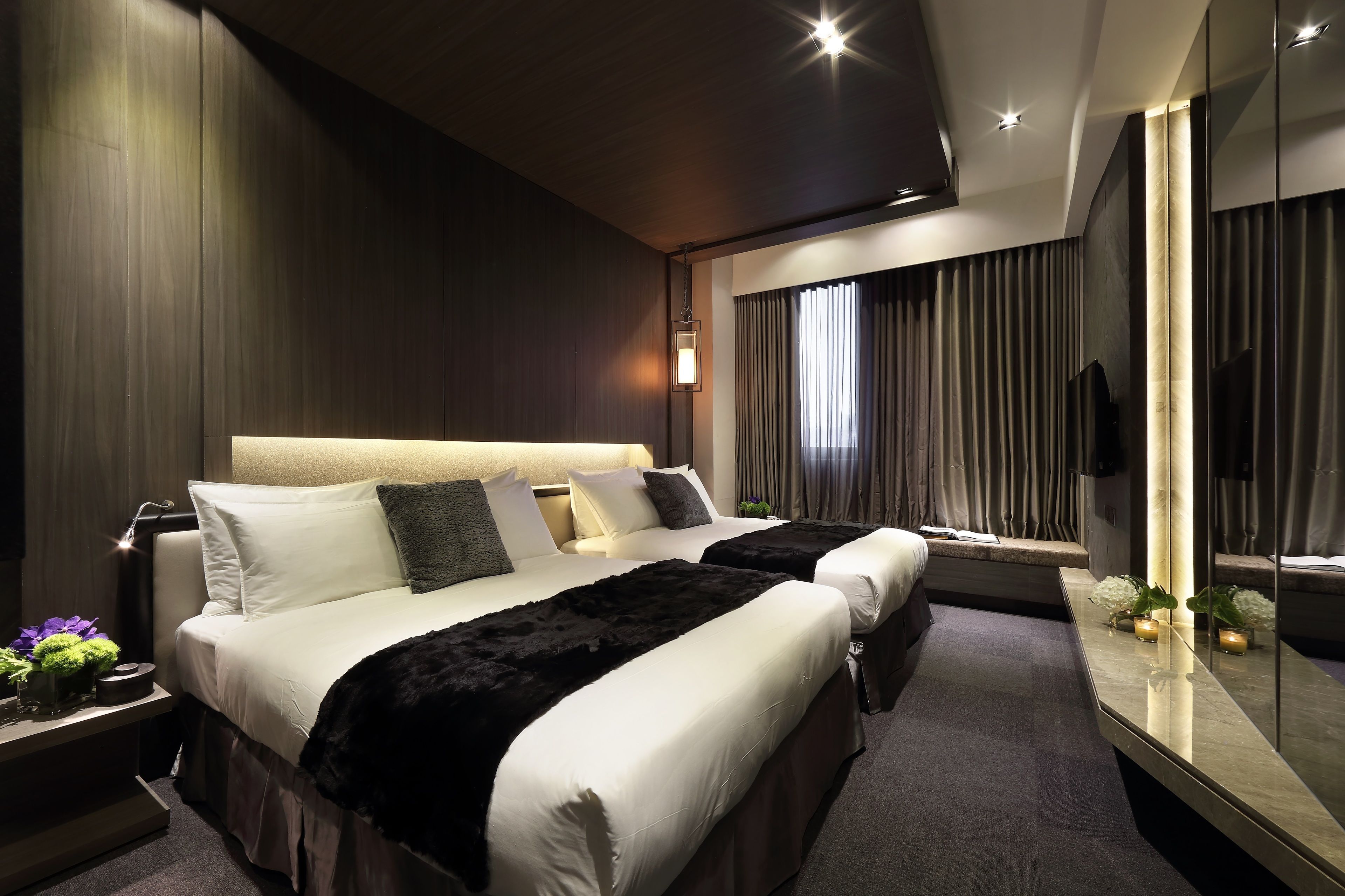 A modern hotel room with two beds, a large mirror, and a nightstand with a lamp.