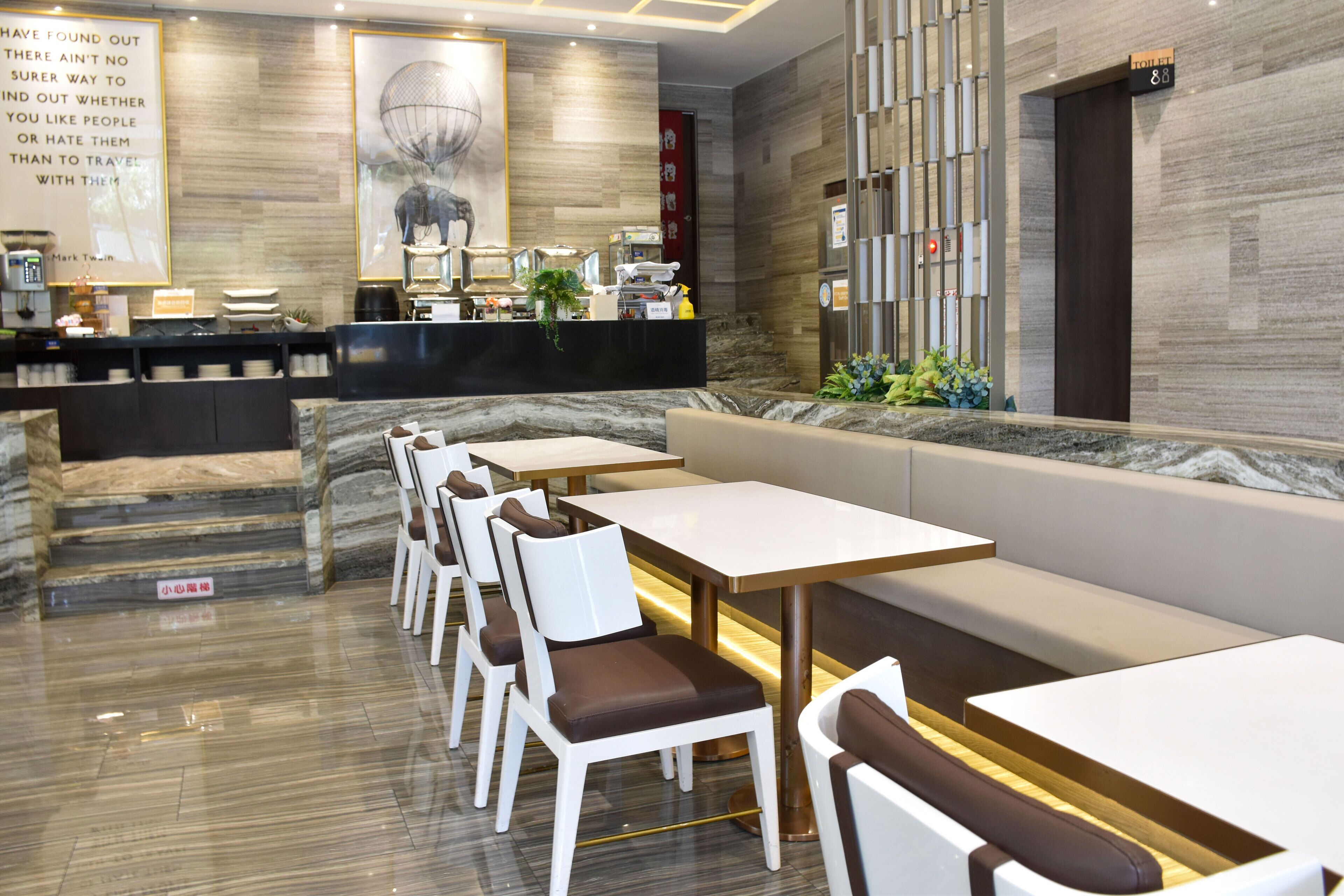 Un restaurant modern amb sòcols de marbre, seients blancs i marrons, una barra amb una màquina de cafè i un mural gran a la paret.