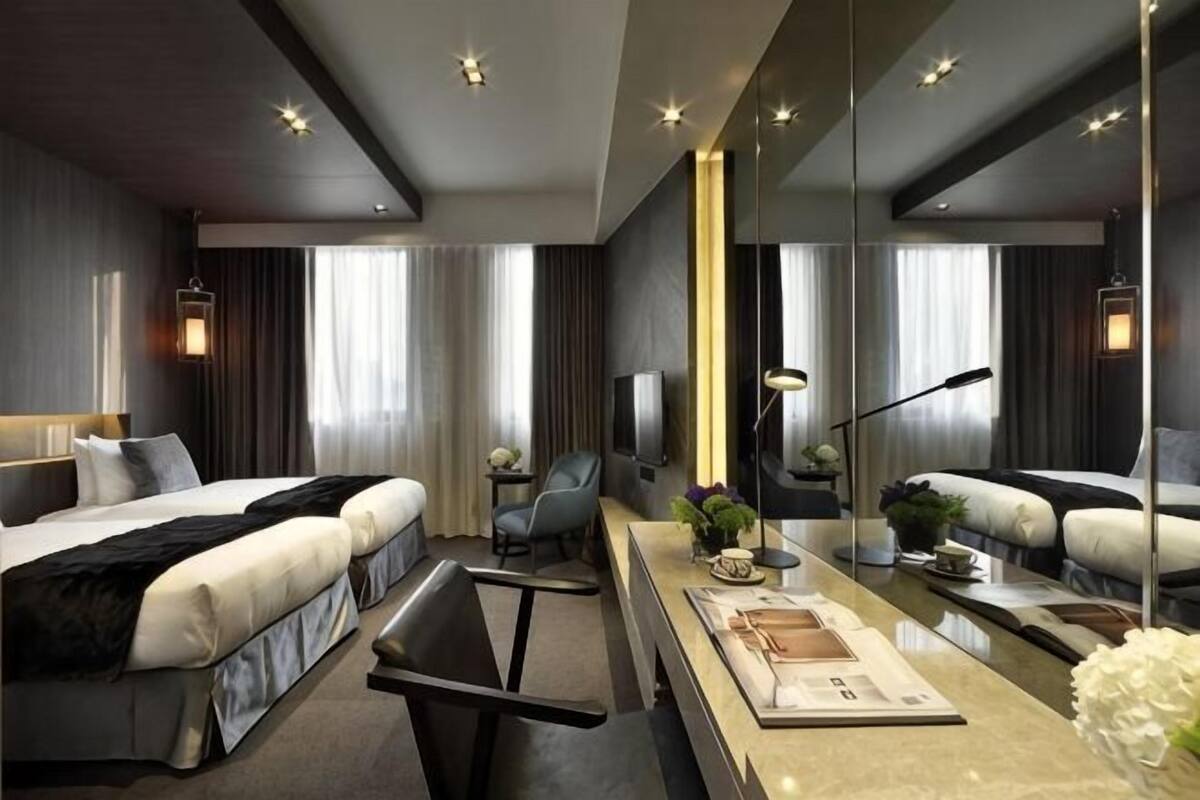 A modern hotel room with a large bed, a desk with a computer, a chair, and a TV.