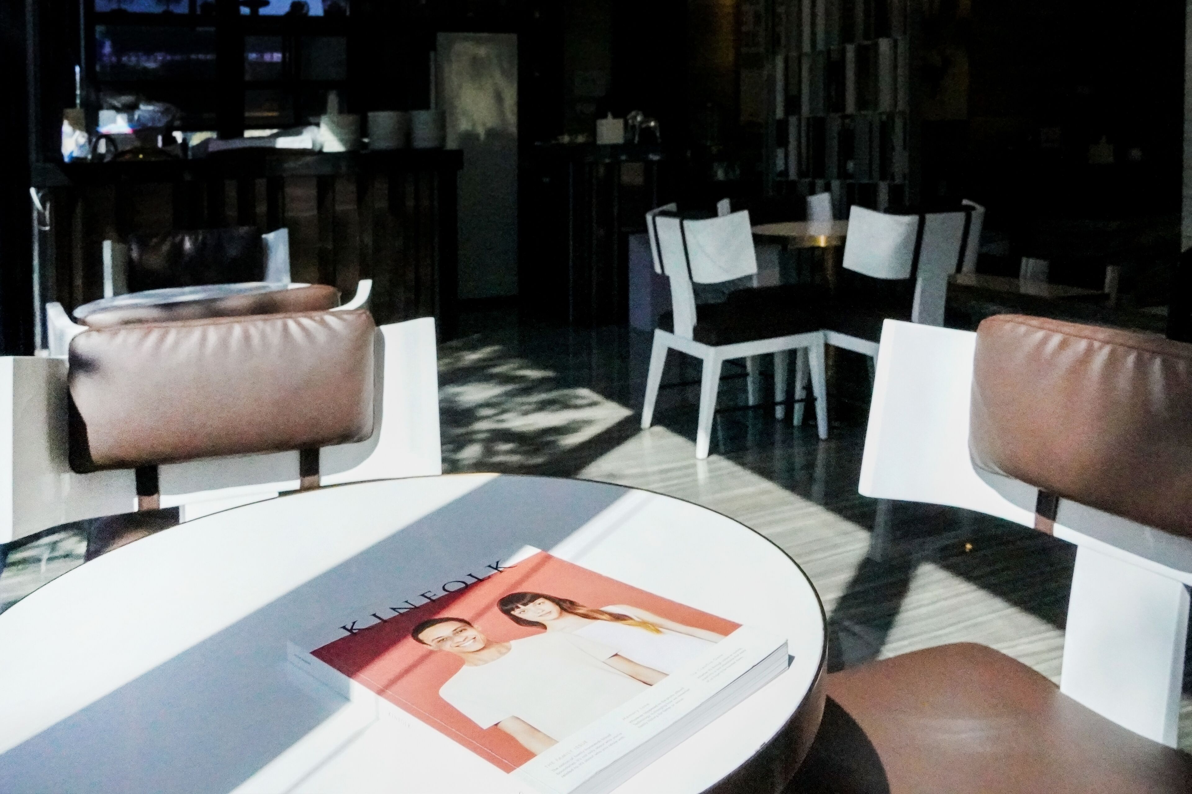 A modern interior with a round table displaying a magazine, leather chairs, and a bar area in the background.