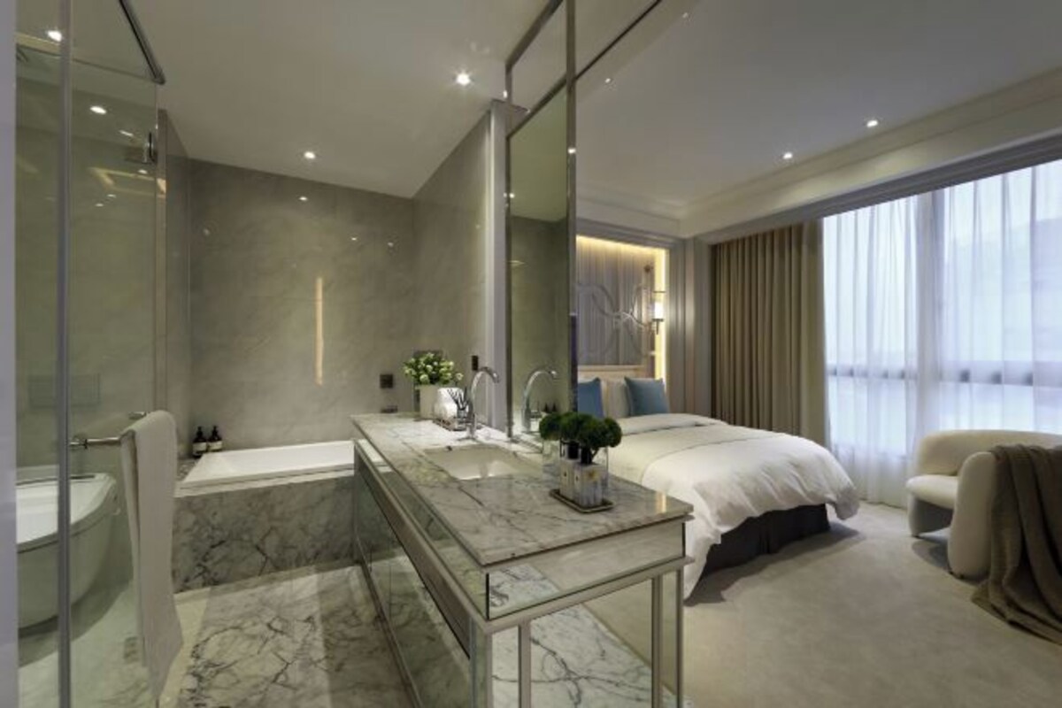 Habitación de hotel moderna con baño de mármol, una cama grande y un área de descanso.