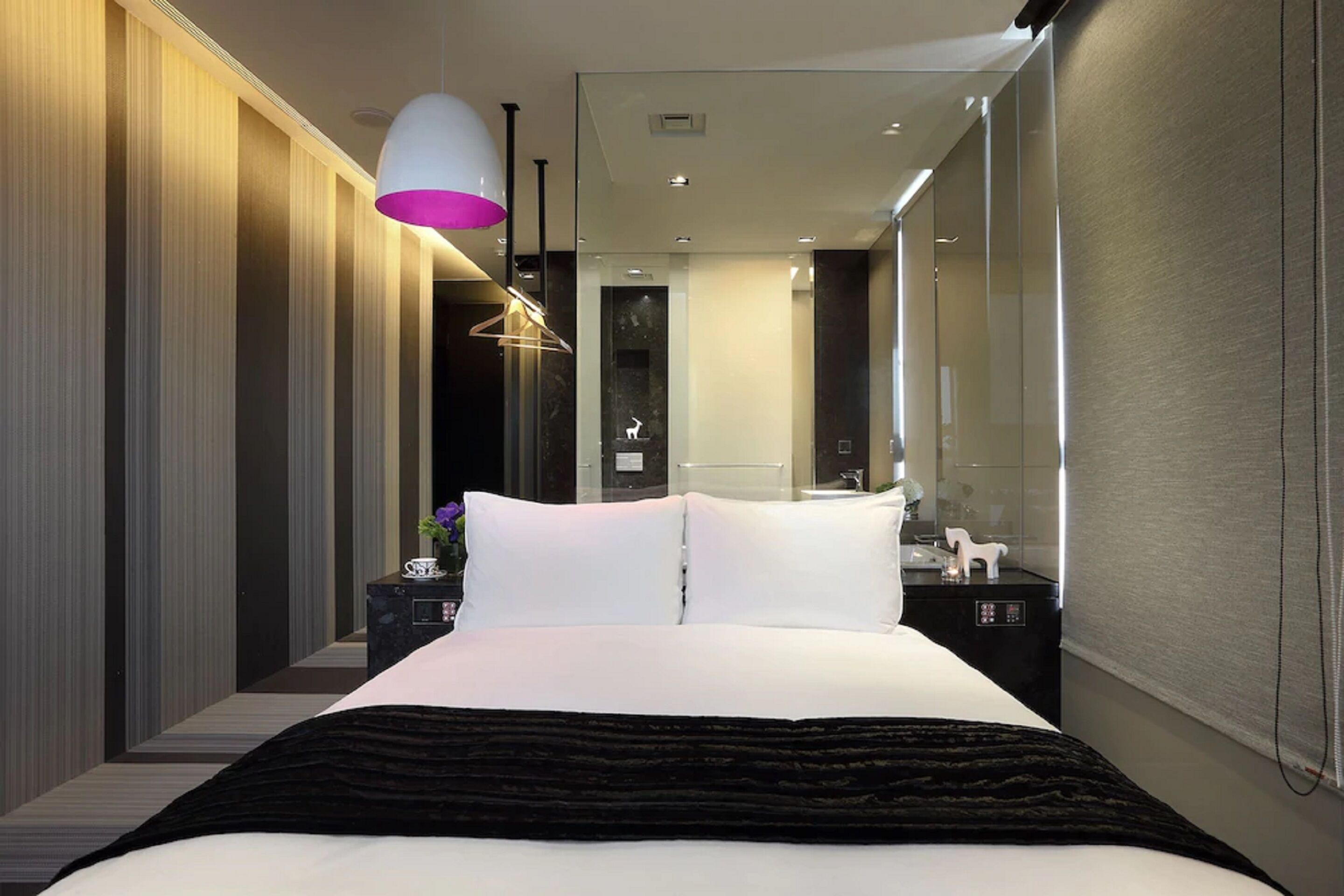 A modern hotel room with a large bed, a bedside table, a mirror, and a decorative lamp.