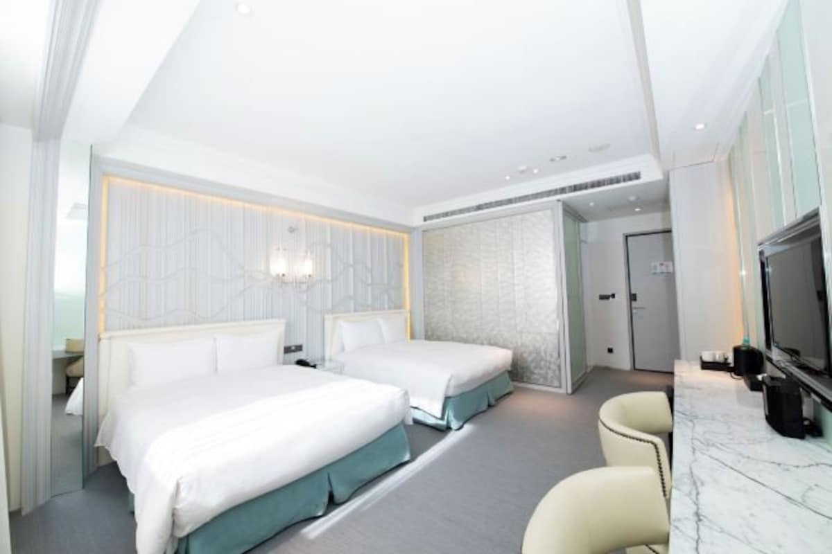 Habitación de hotel con dos camas, televisión y encimera de mármol.