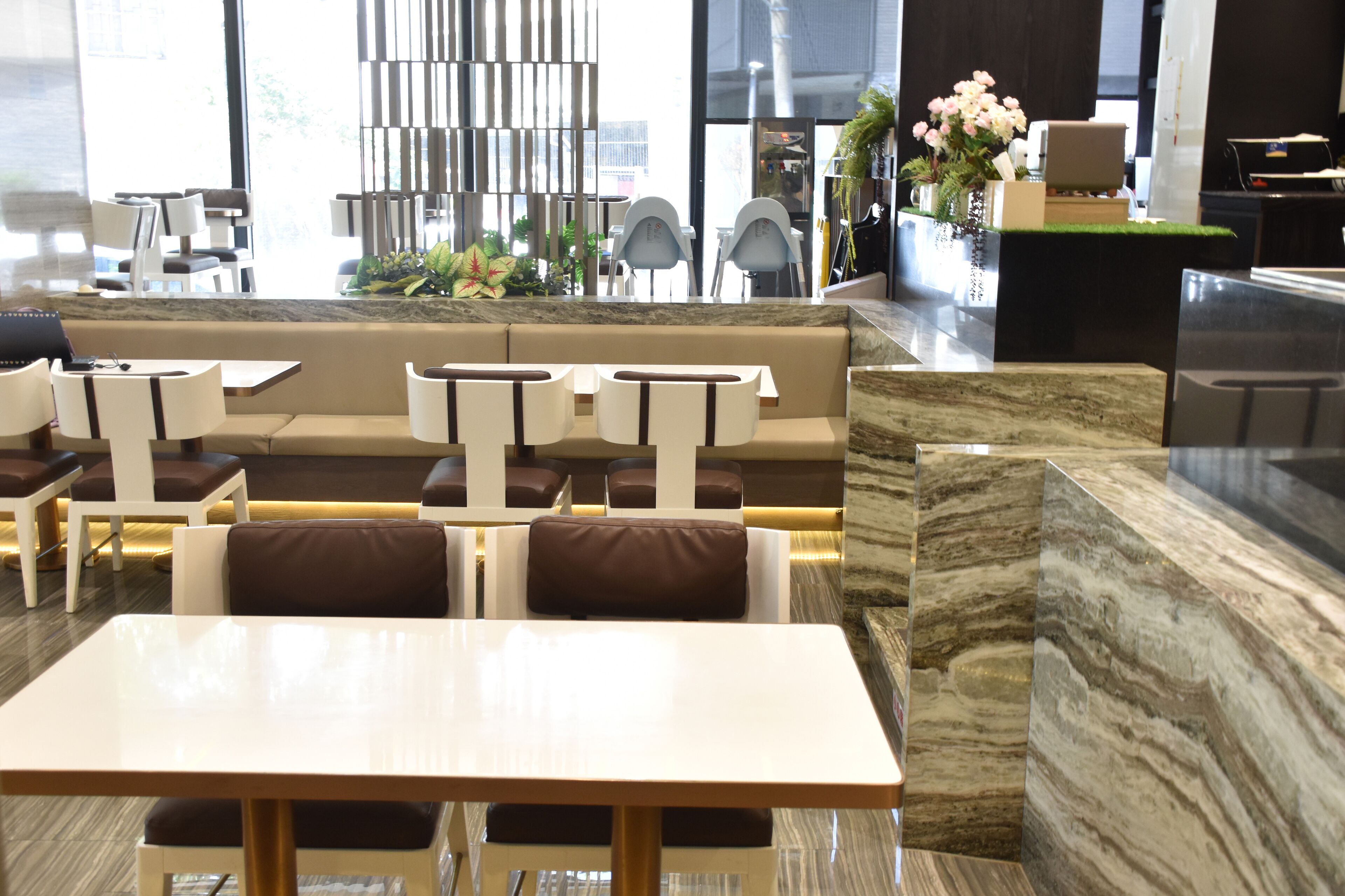 A modern restaurant with marble flooring, white and brown seating, and a central decorative wall.