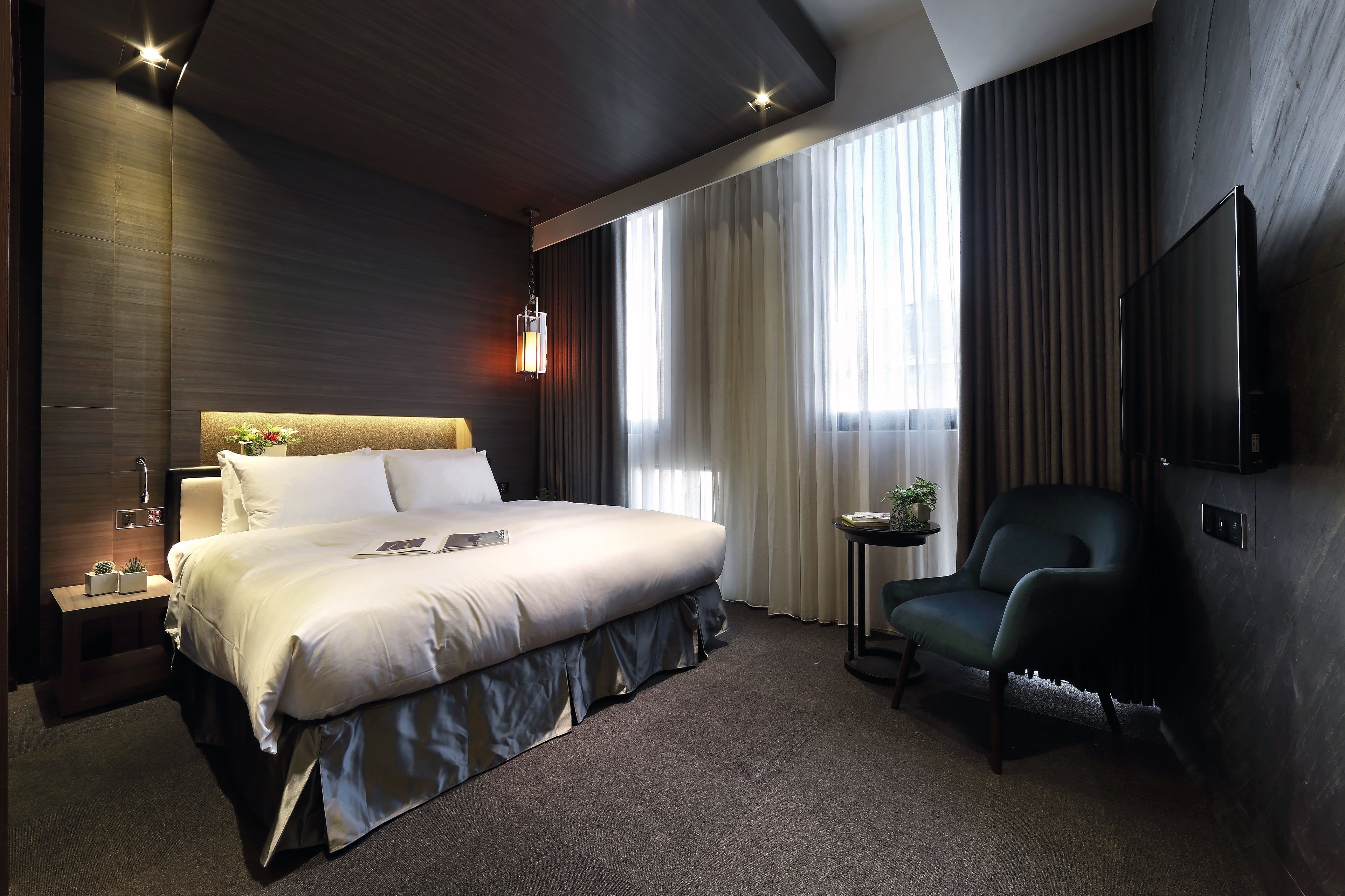 A modern hotel room with a large bed, a desk, a chair, and a TV on the wall.