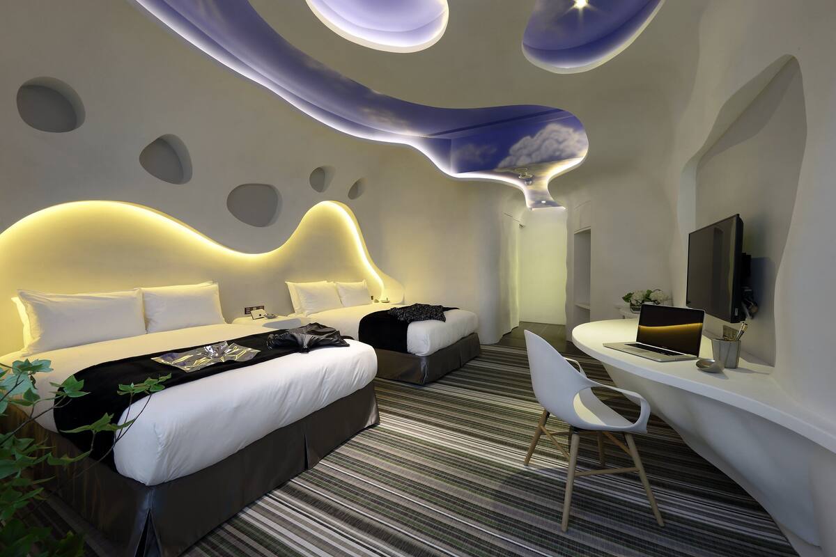 A modern hotel room with a large bed, a desk with a laptop, and a TV.
