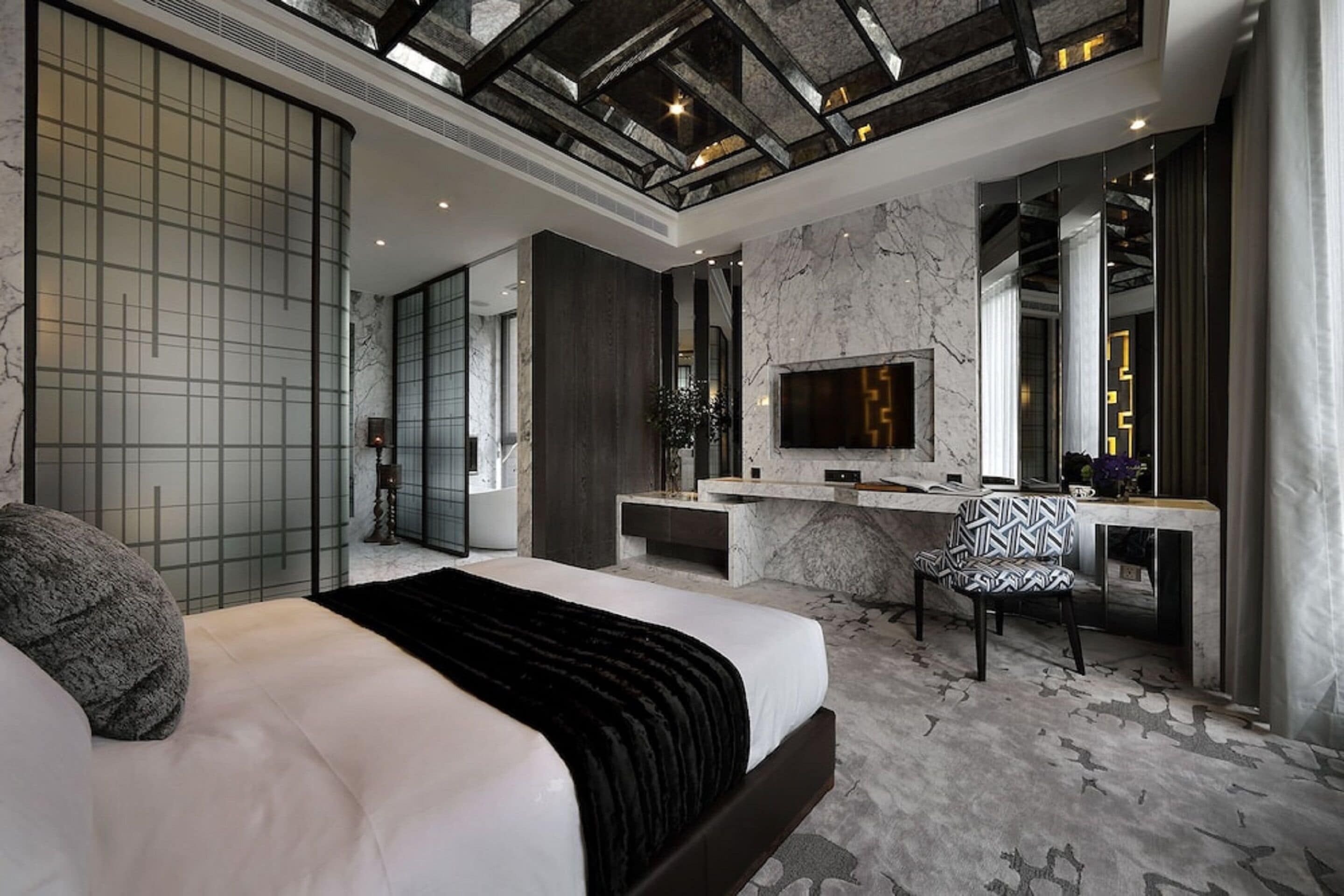 A modern bedroom with a large bed, a desk, and a TV.