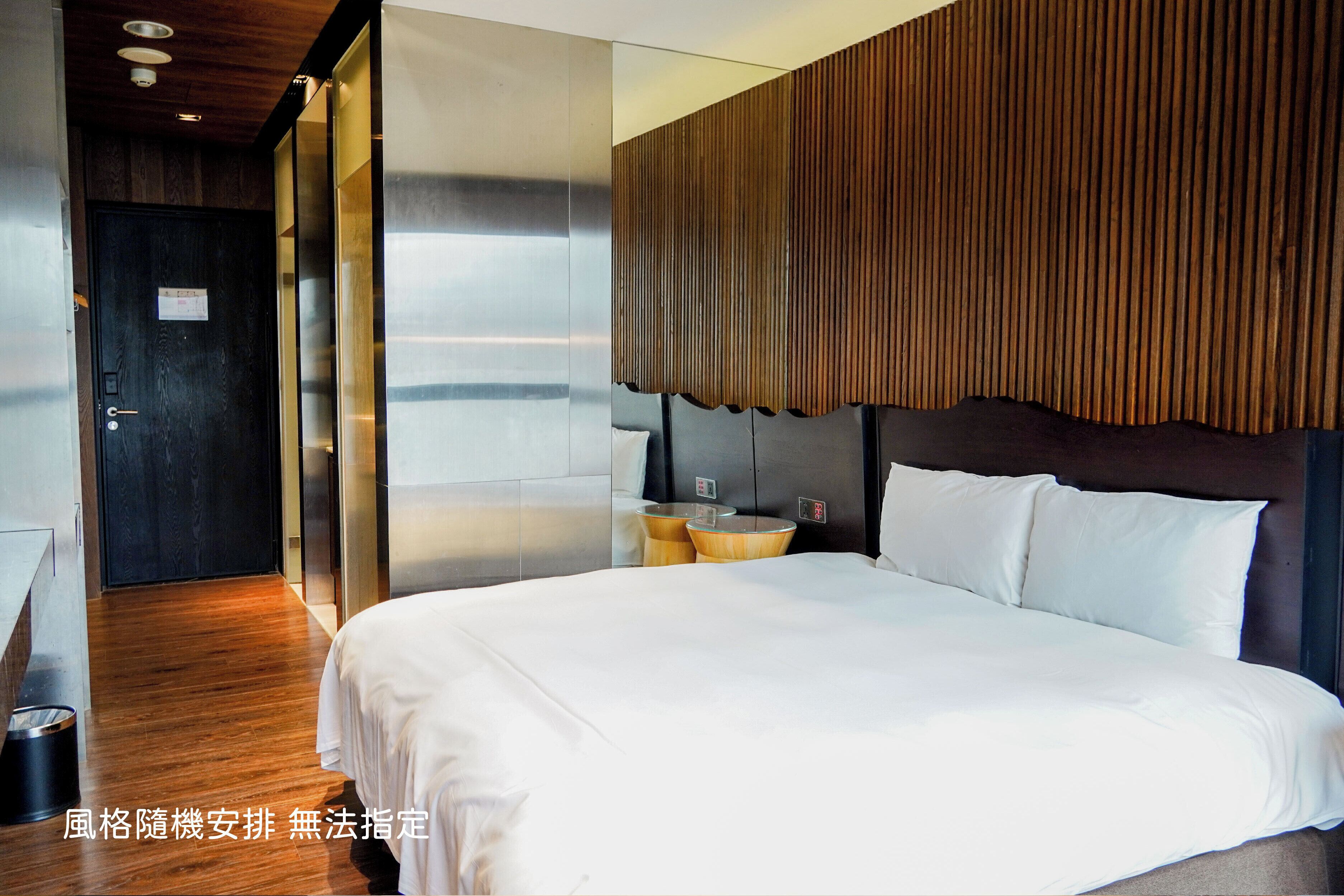 A modern hotel room with a large bed, a wooden headboard, and a view of the sea.