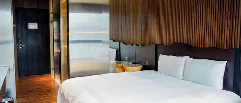 A modern hotel room with a large bed, a wooden headboard, and a view of the sea.
