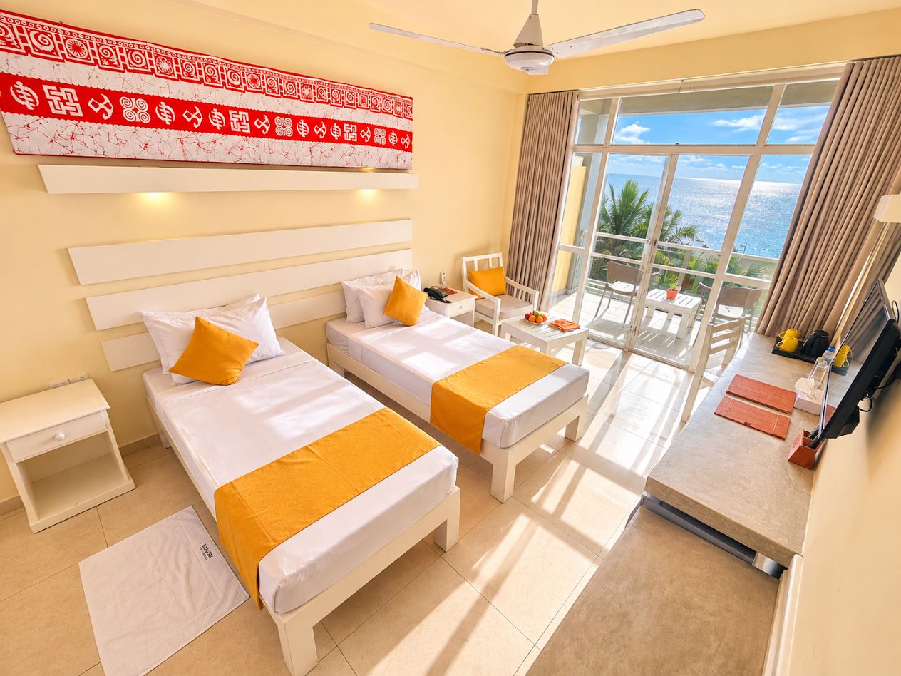 A hotel room with two beds, a balcony with a view, and a desk with a chair.