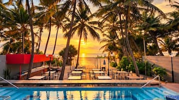 A swimming pool with palm trees and a sunset view.