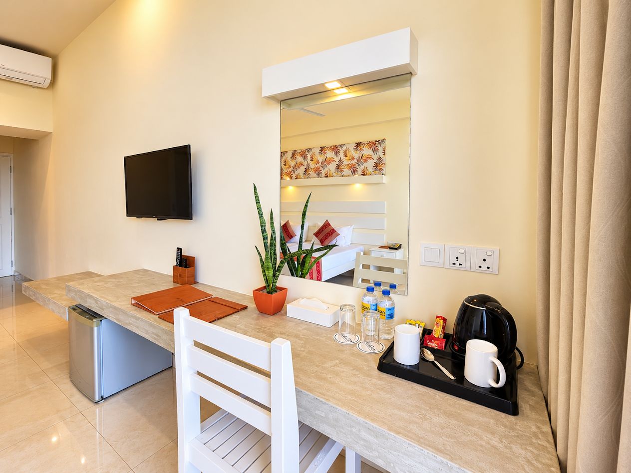 Una cocina moderna con una televisión de pantalla plana, un refrigerador pequeño, una mesa de comedor con sillas, una cafetera y una planta en maceta.