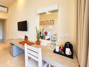 A modern kitchen with a flat-screen TV, a small refrigerator, a dining table with chairs, a coffee maker, and a potted plant. - Beacon Beach Hotel (Negombo)