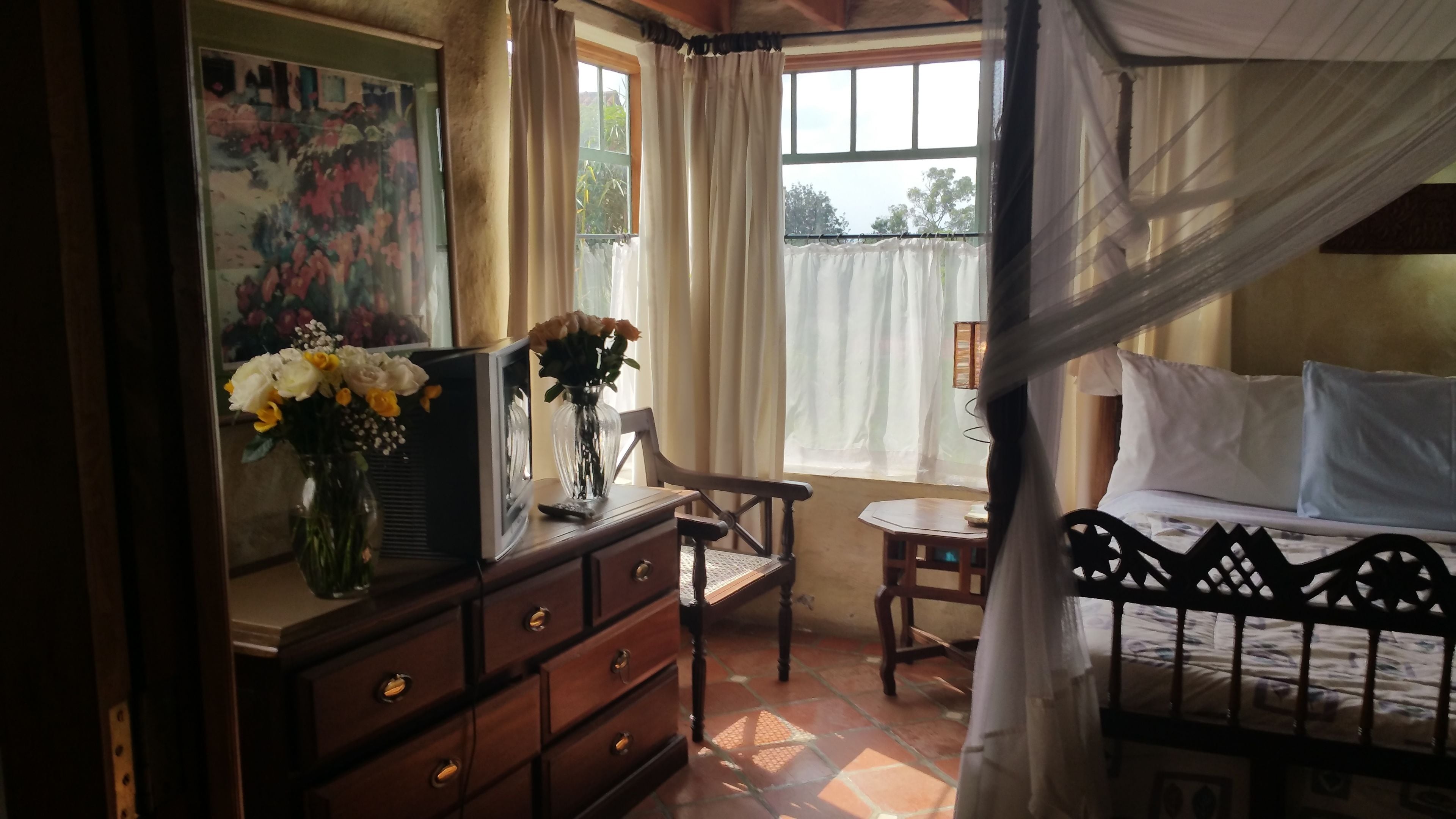 A bedroom with a bed, a nightstand, a dresser, a chair, a window with curtains, and a painting on the wall.