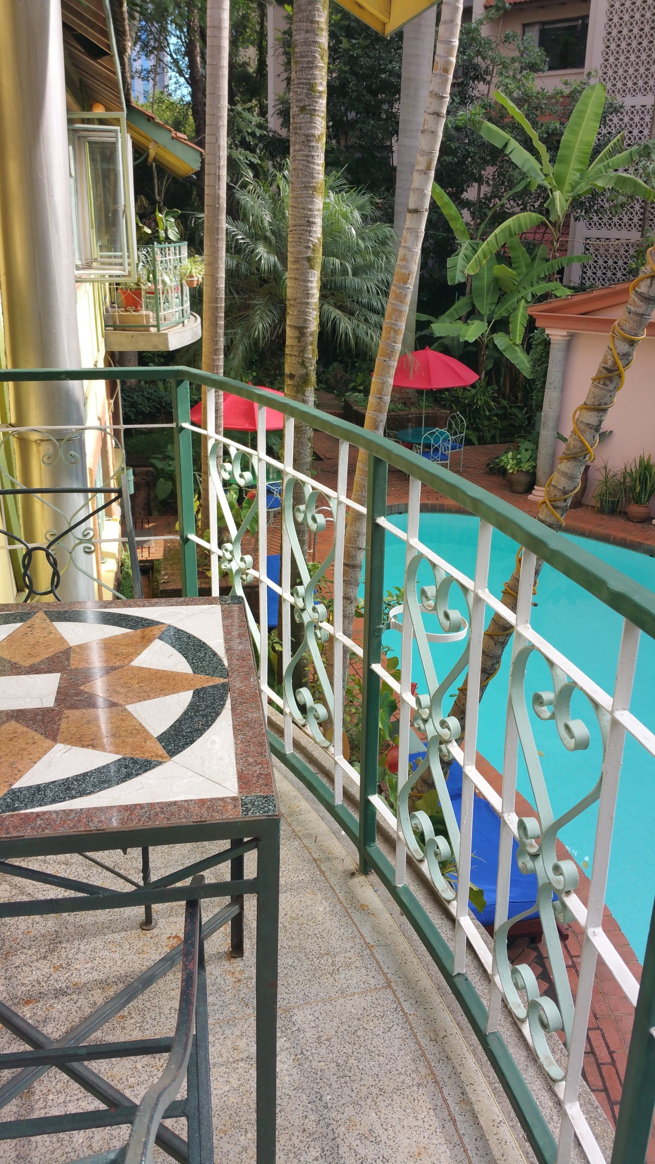 Un balcon doté d’un sol carrelé, d’une rambarde en métal et offrant une vue sur une piscine.