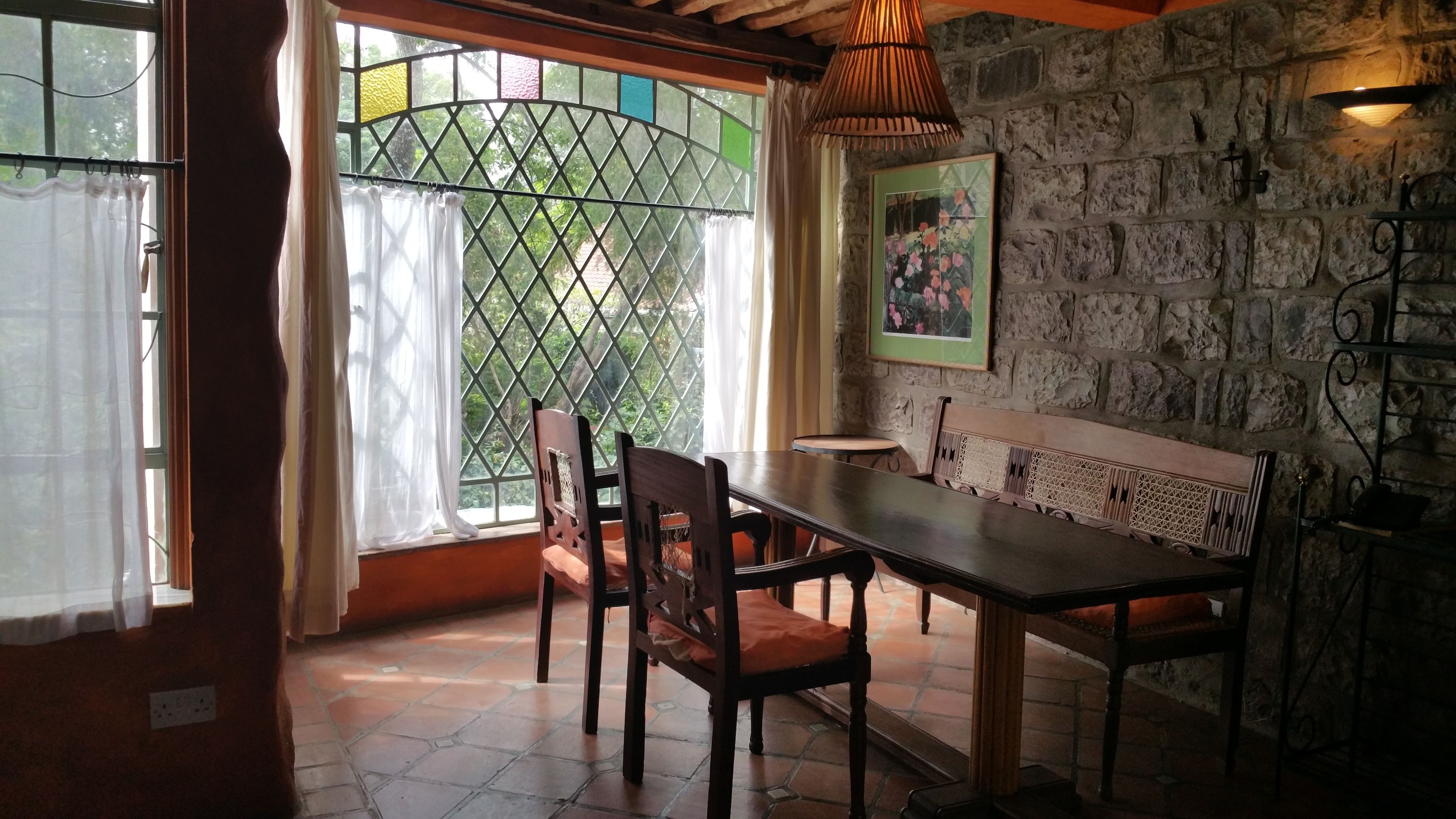 Un comedor con mesa y sillas de madera, un banco, una pared de piedra y una ventana con celosía.