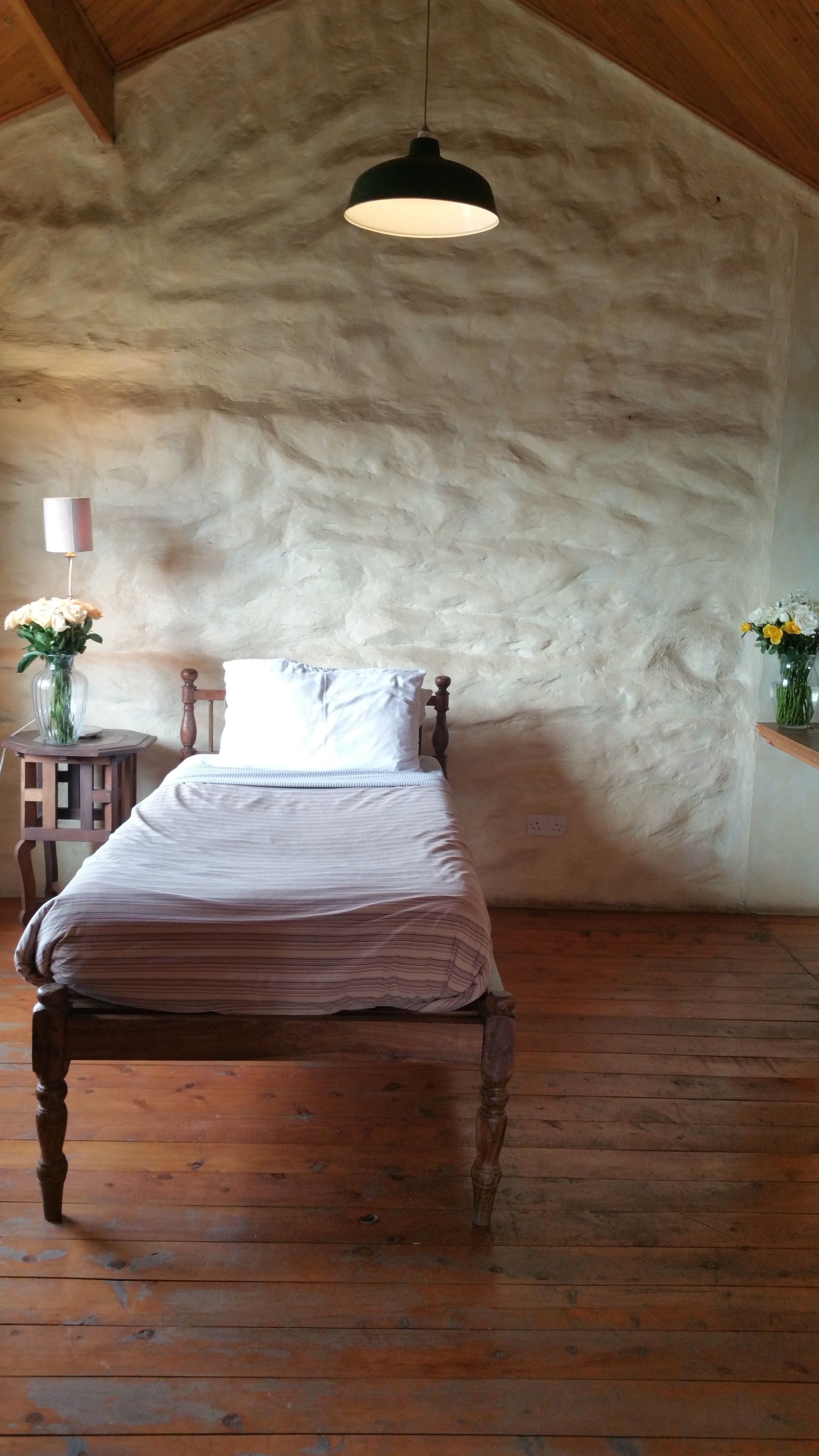 Une chambre avec un lit en bois, un luminaire suspendu et un mur en pierre à la texture particulière.