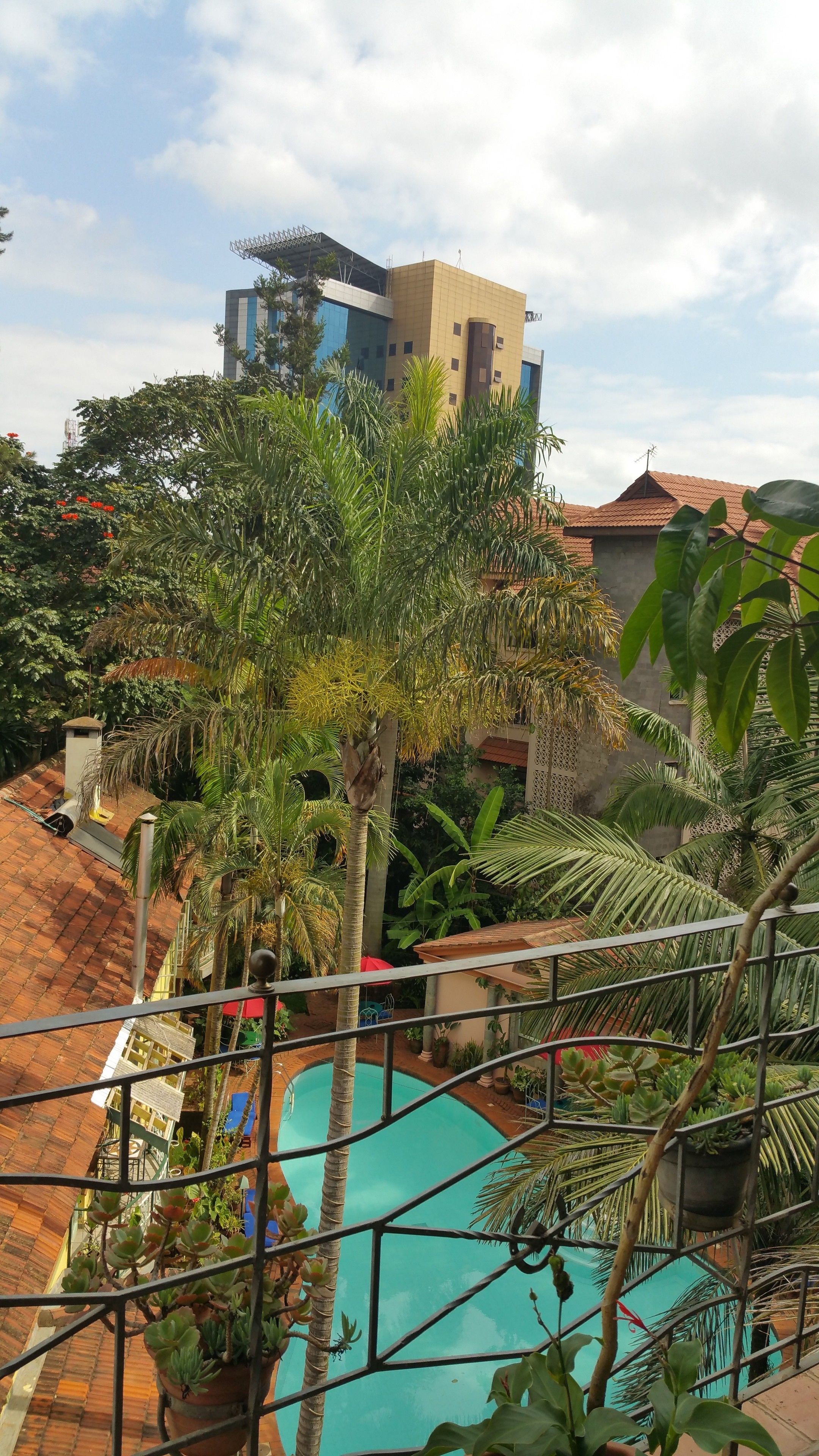 Uma área de piscina rodeada por vegetação exuberante e um edifício com telhado cerâmico ao fundo.