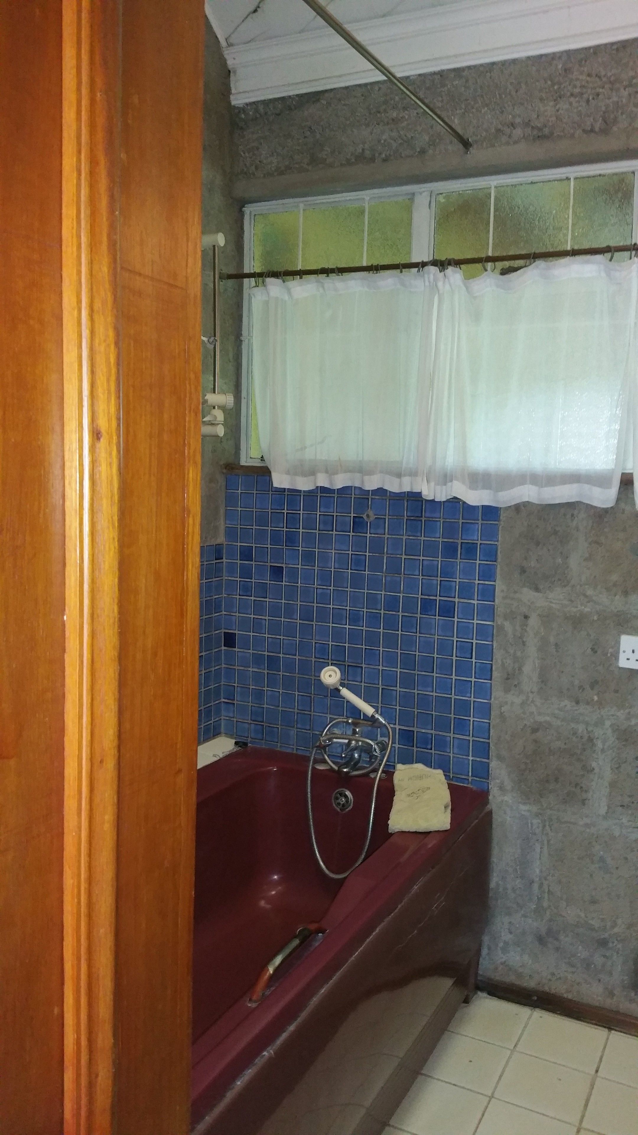 A bathroom with a red bathtub, blue tiled walls, a white shower curtain, and a wooden door.
