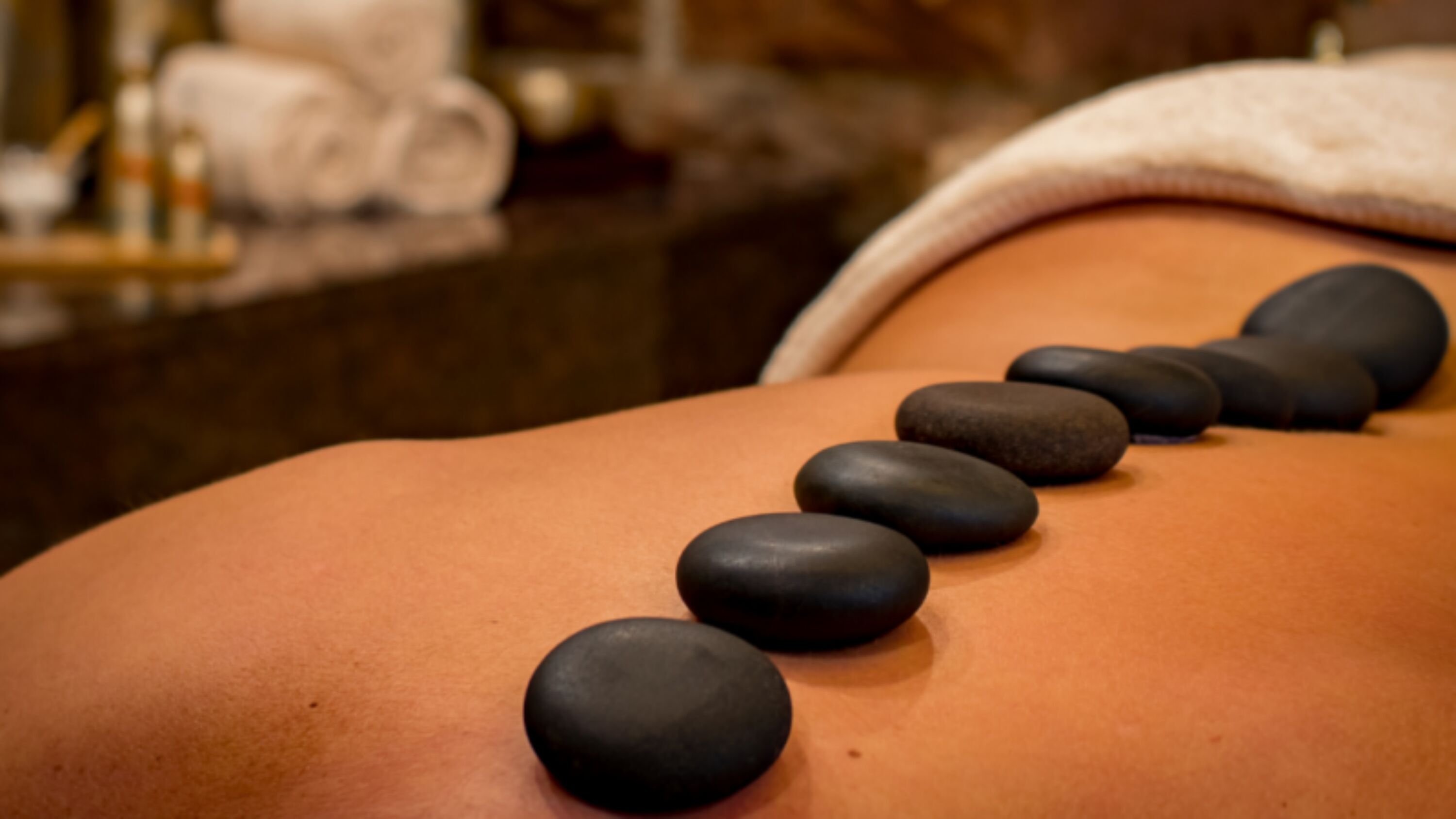 A massage therapy session with black stones placed on a person's back.