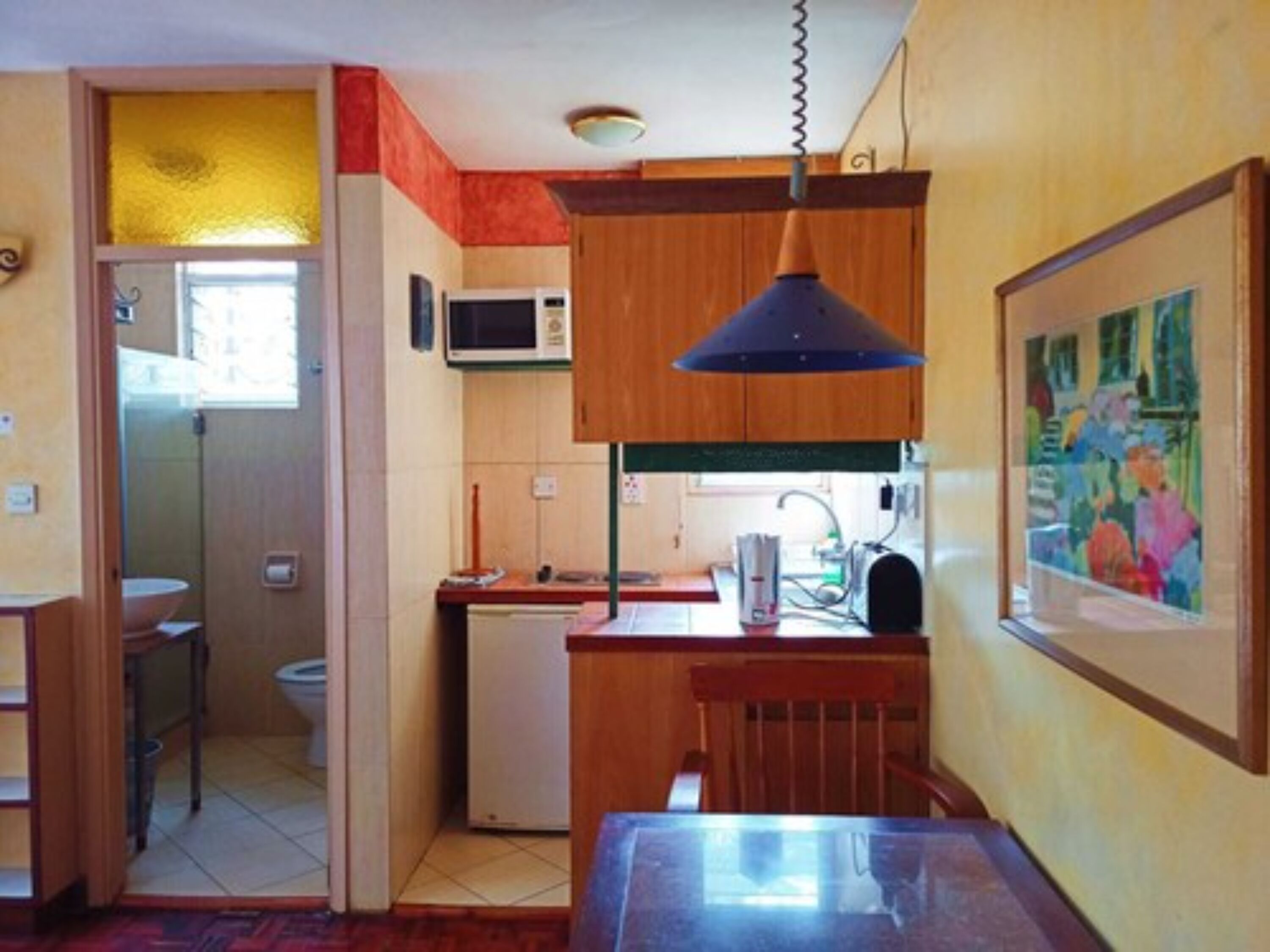 A compact kitchen with wooden cabinets, a microwave, a sink, and a dining area with a table and chairs.