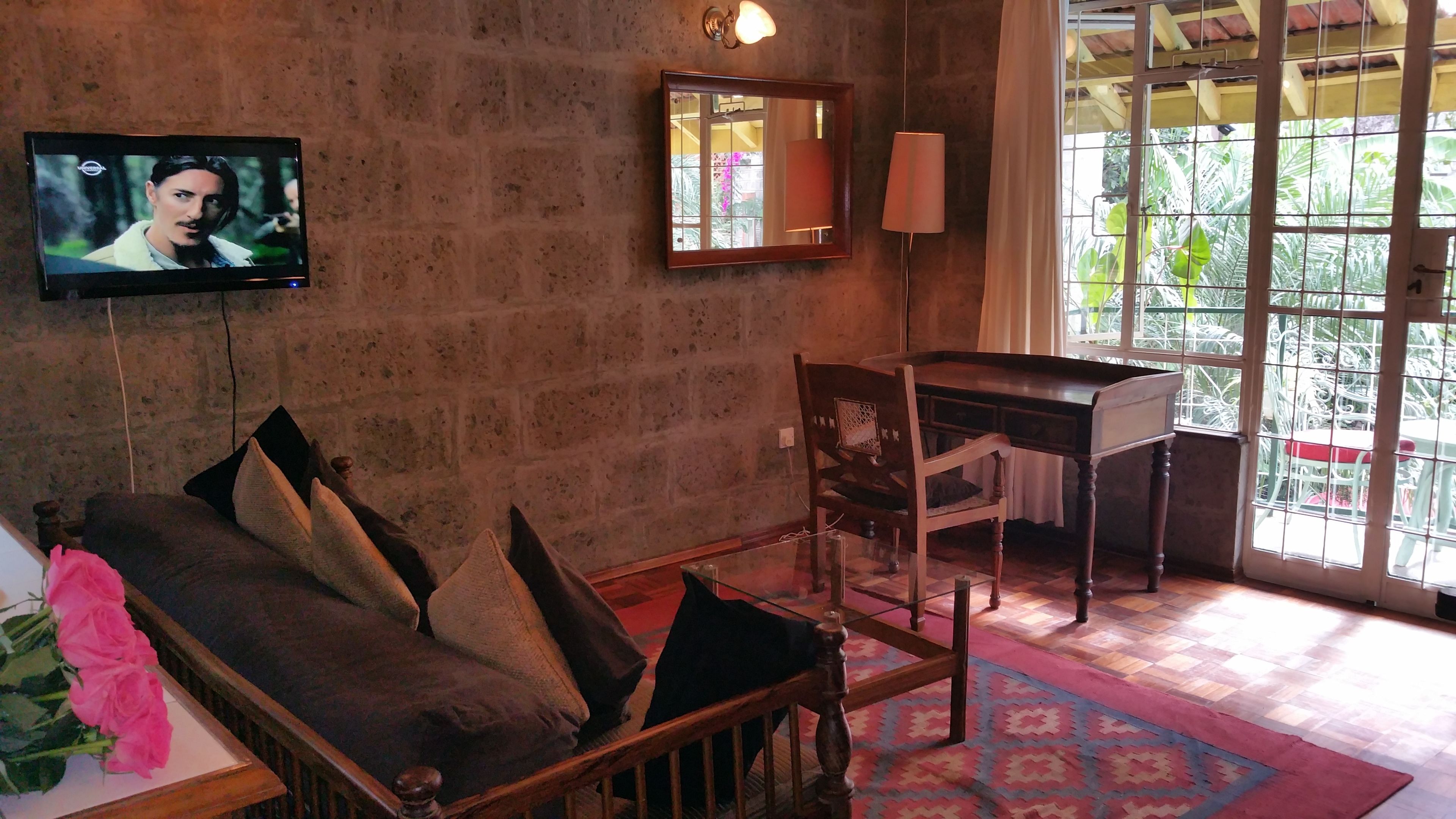 A living room with a sofa, a wooden table, a mirror, a TV, and a window with a view of greenery.