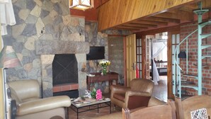 A cozy living room with a stone fireplace, leather chairs, a coffee table, and a staircase with a wooden railing. - Woodmere Serviced Apartments (Nairobi)