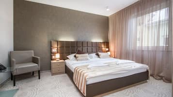 A modern hotel room with a large bed, a nightstand, a chair, and a desk with a computer.