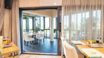 Habitación de hotel moderna con puerta de vidrio corredera que da a un comedor con sillas blancas y una mesa.