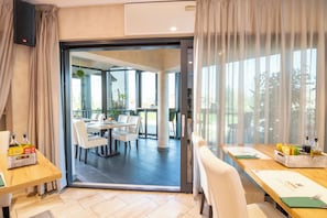Habitación de hotel moderna con puerta de vidrio corredera que da a un comedor con sillas blancas y una mesa.
