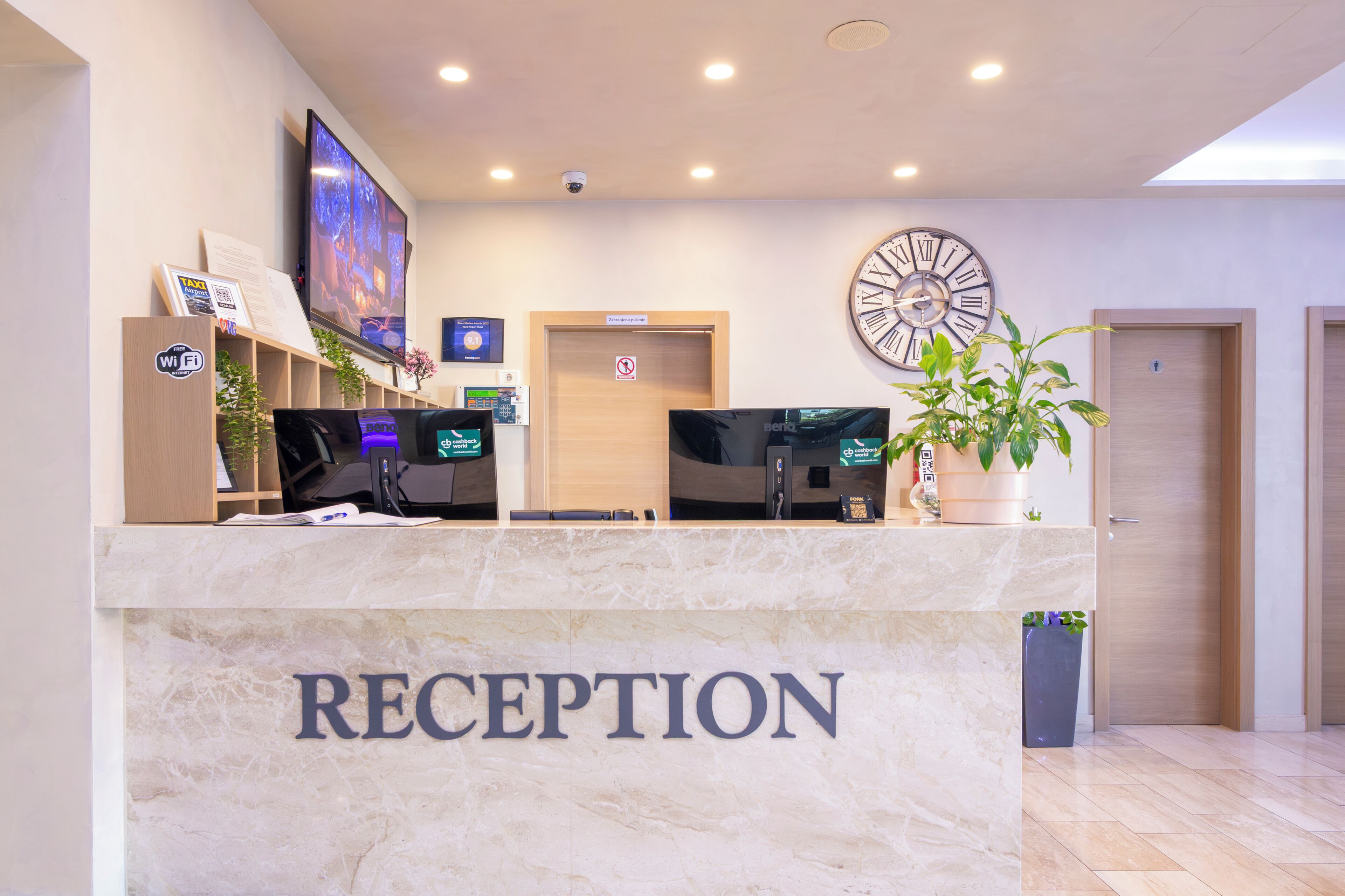 A reception desk with a 'RECEPTION' sign, a clock, a TV, and a plant.
